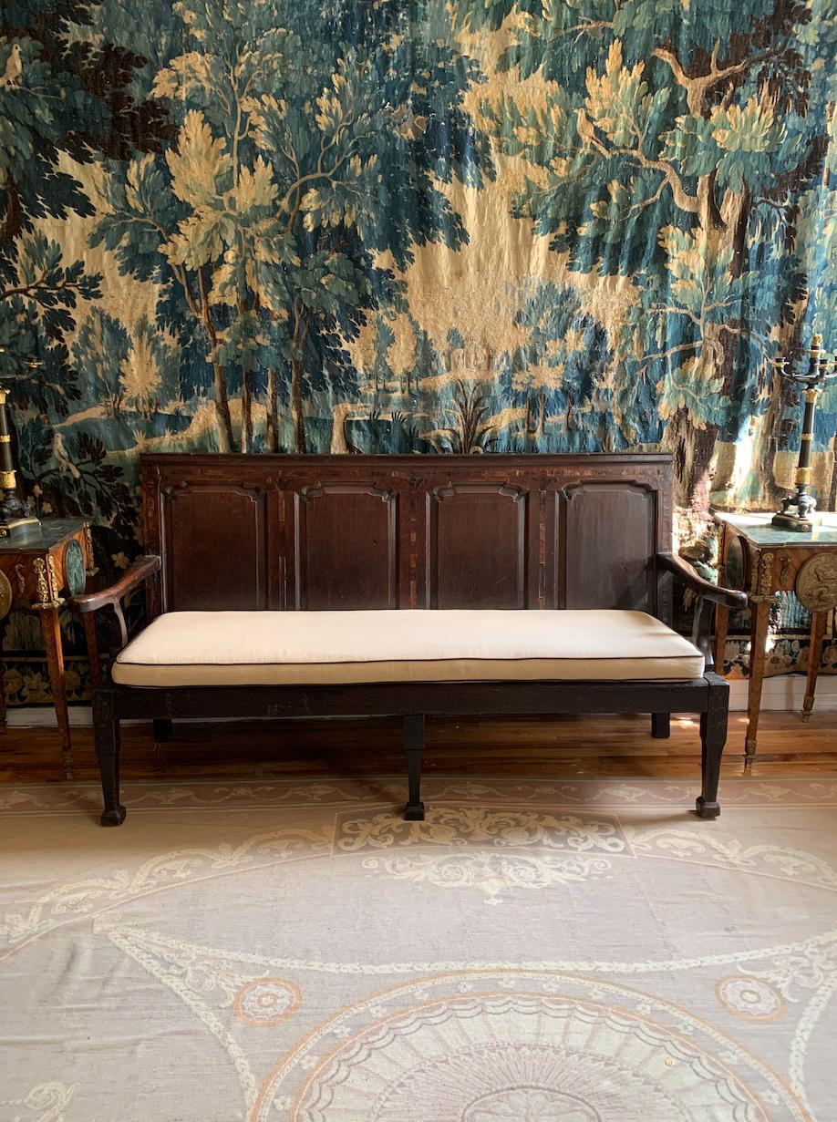 A handsome English settle bench with a shaped four-panel back. The back mullions are inlaid with foliate design resembling a fleur de lis. A deep comfortable seat sports a modern foam upholstered cushion with chocolate colored piping. England, c.
