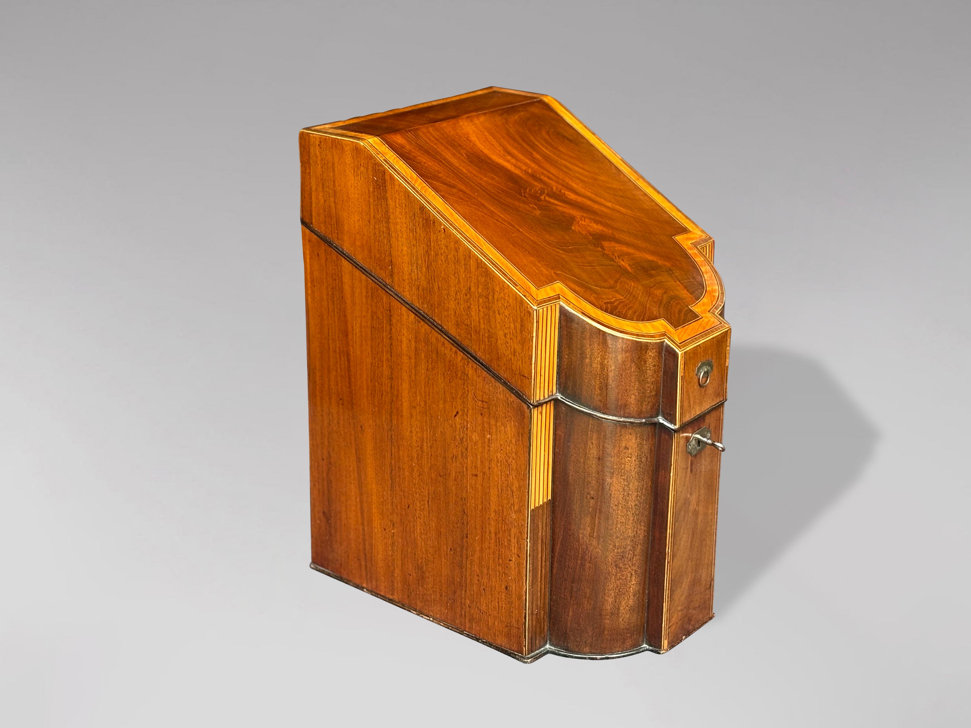 Fina caja o cantimplora de cuchillos de caoba de finales del siglo XVIII, época de Jorge III, con interior ajustado. Tapa inclinada sobre frente de serpentina con bandas transversales de madera satinada y cordones de palisandro y ébano. De