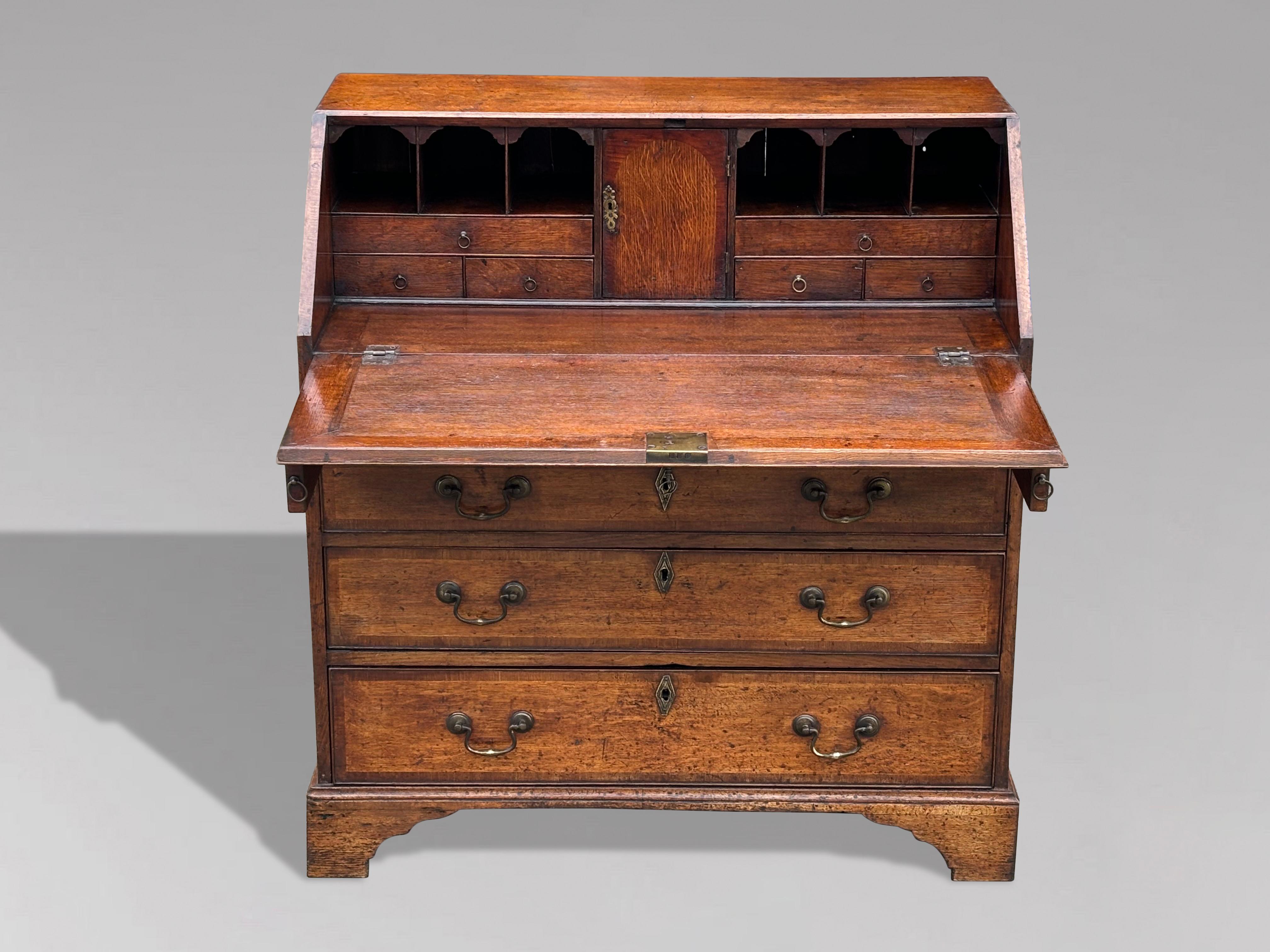 This charming late 18th-century George III period oak bureau showcases exquisite craftsmanship and timeless appeal. The fall front opens to reveal a well-organized interior, featuring pigeonholes and drawers, along with a concealed well for added