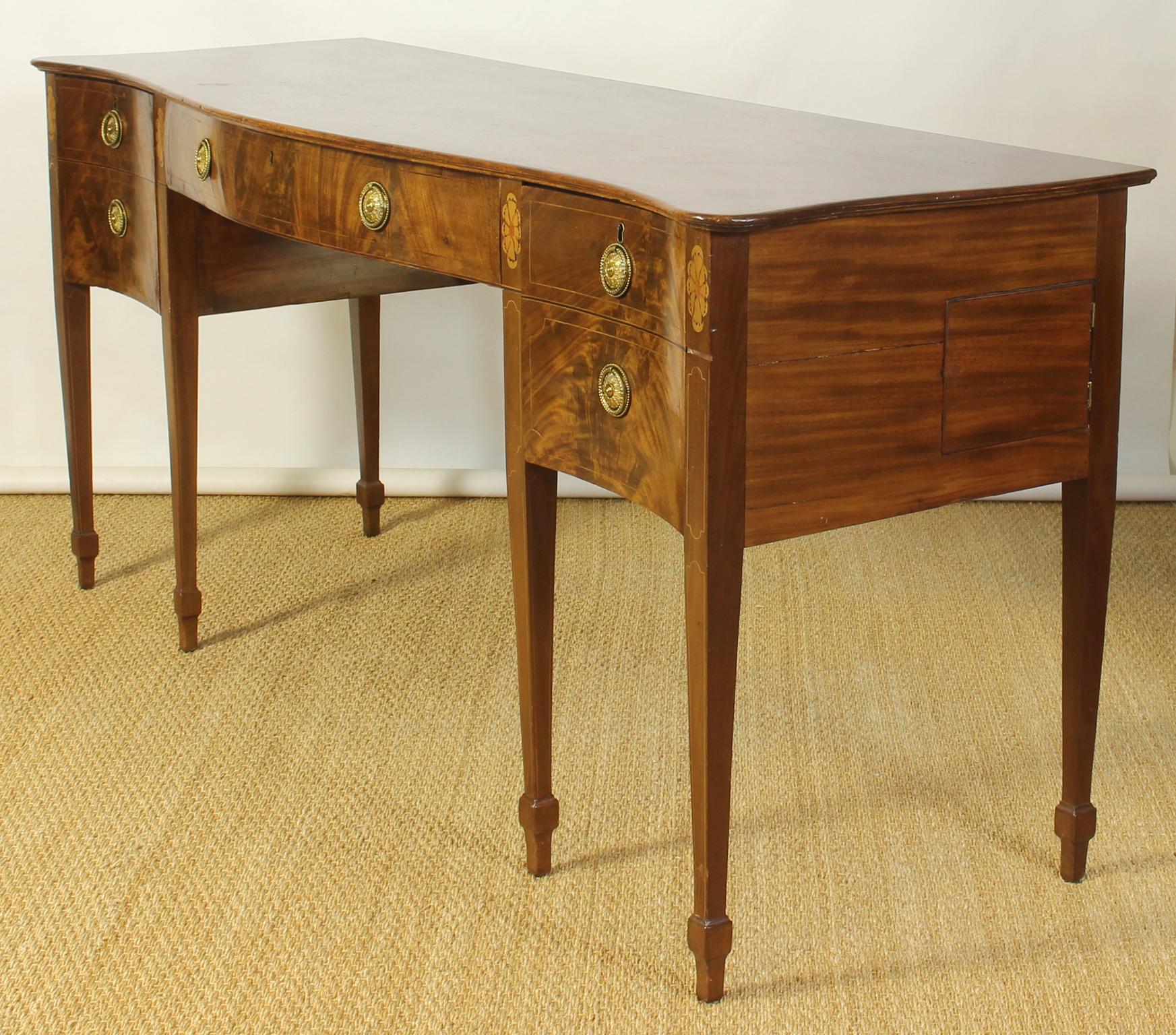 An exceptionally long and elegantly proportioned late 18th century. English serpentine front Geo. III mahogany sideboard with one centre drawer and two flanking cabinets accented with original gilt brass pulls.