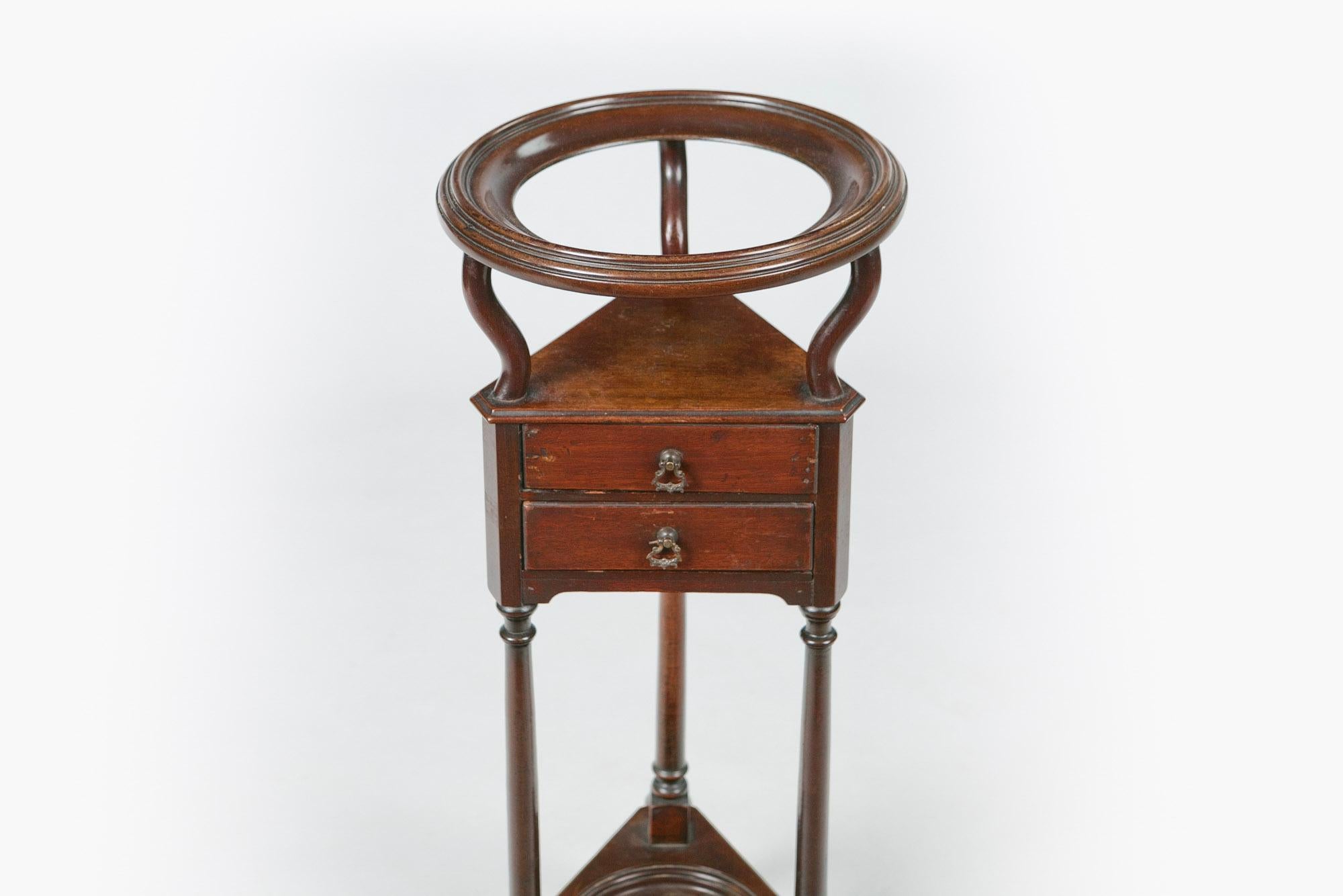 18th century George III mahogany wash or wig stand, the moulded top of circular form with porcelain bowl raised over three curved supports above moulded shelf of triangular form with two drawers with ornate pulls supported on three turned columns