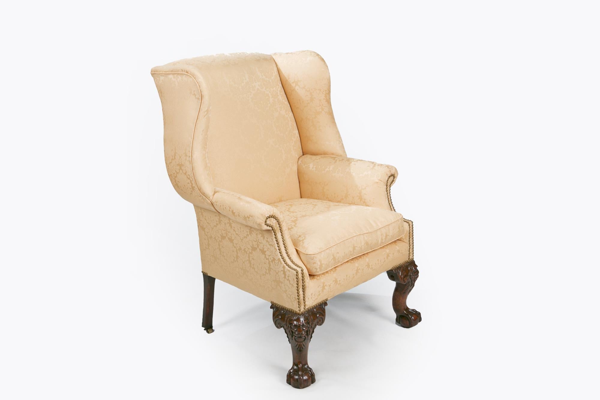 18th century George III wing chair, the straight back with outscrolled wings raised over outscrolling arms raised above hipped cabriole leg with lion mask on knee flanked with scrolling foliate carved in high relief terminating on ball and claw foot.
