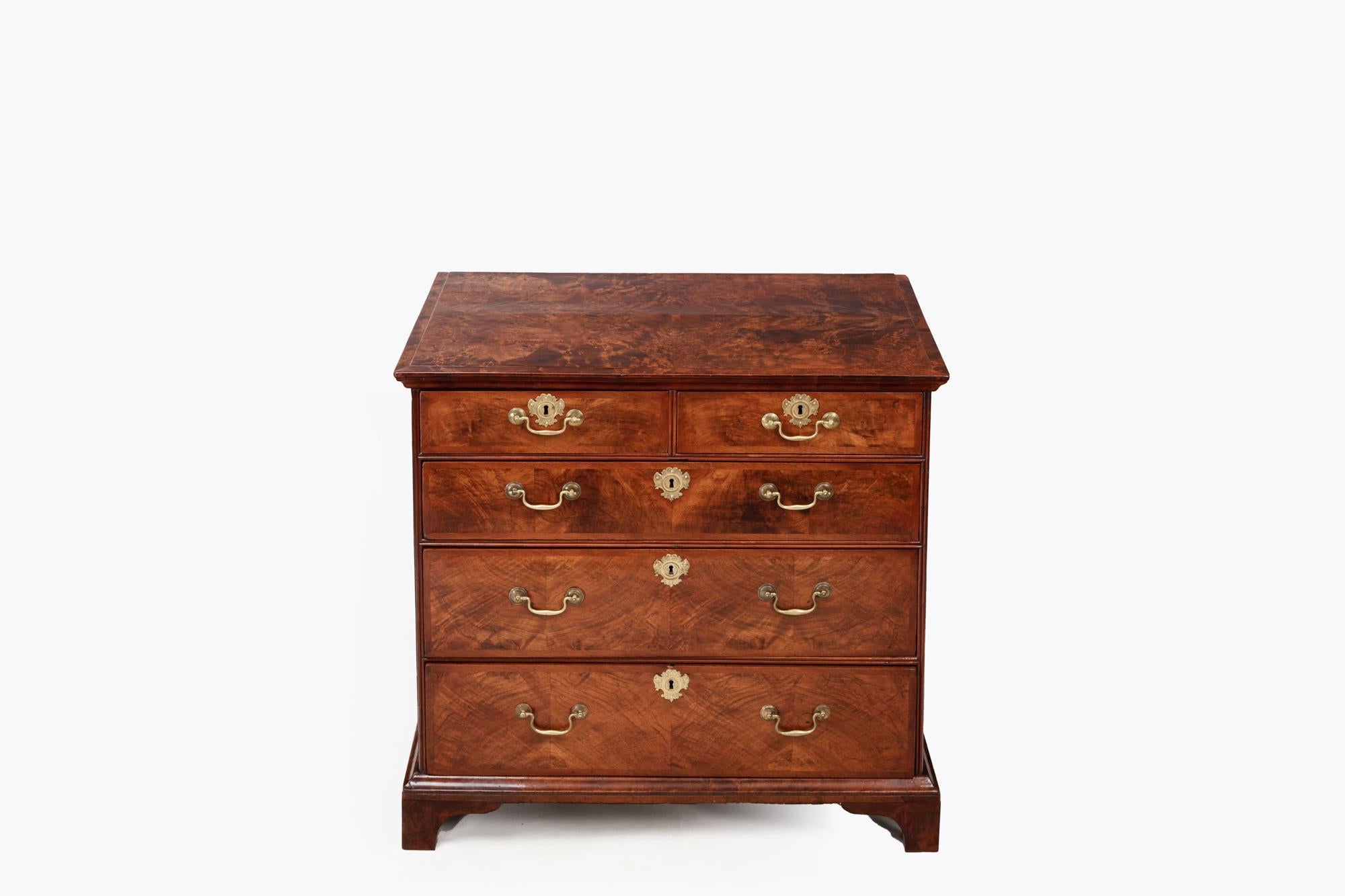 18th Century Georgian Burr Walnut Chest of Drawers with original ornate brass escutcheons, and swan neck handles. Featuring five drawers and simple ogee bracket feet. 