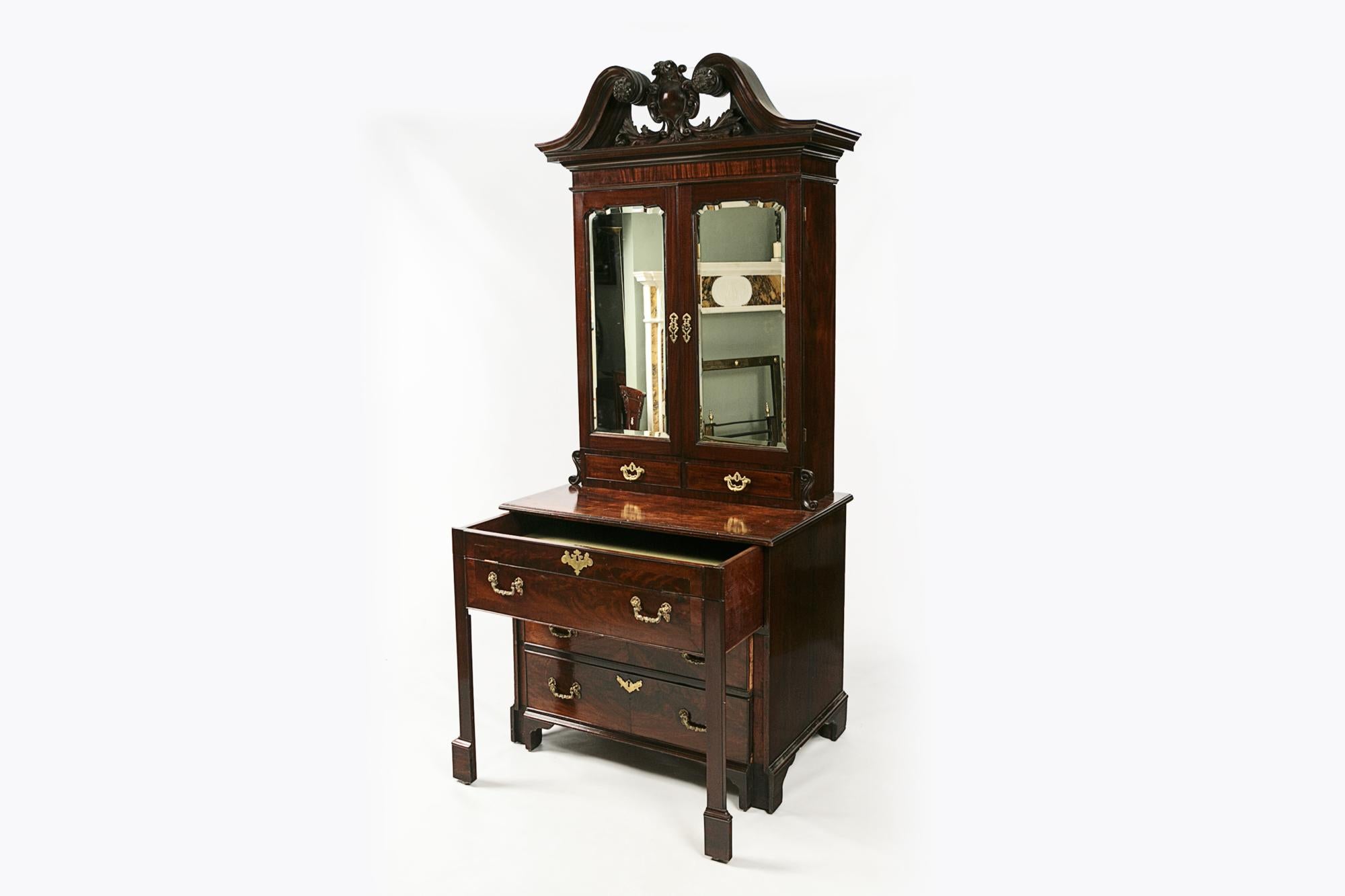 18th Century Georgian Cuban flame mahogany estate cabinet secretaire with stepped molded cornice surmounted by a swan-neck pediment with a centered acanthus crest, flanked by carved scroll and sunflower motifs. Dos puertas biseladas de espejo se