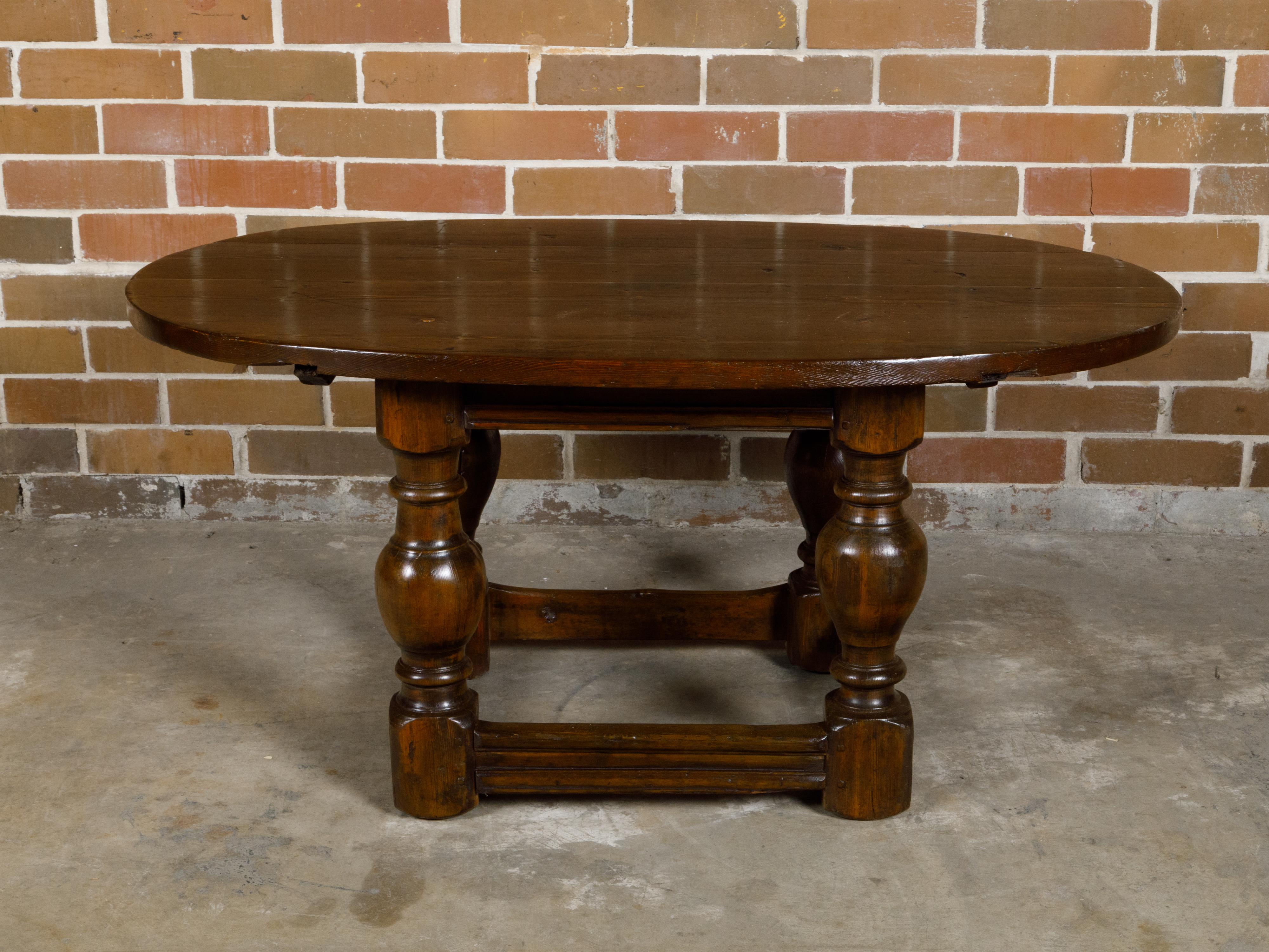 An English Georgian period pine table from the 18th century with oval top, turned legs and side stretchers. This exquisite English Georgian period pine table from the 18th century marries the rustic charm of its material with the refined elegance of