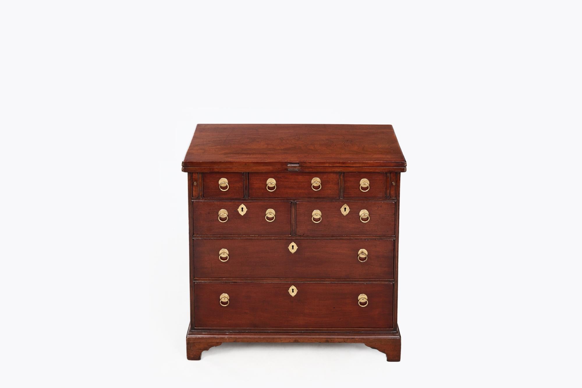 18th Century Georgian mahogany bachelor’s chest with original brass ring handles and escutcheons. Featuring fold-over top, pull-out leaf supports, and seven drawers. Raised on simple ogee bracket feet.