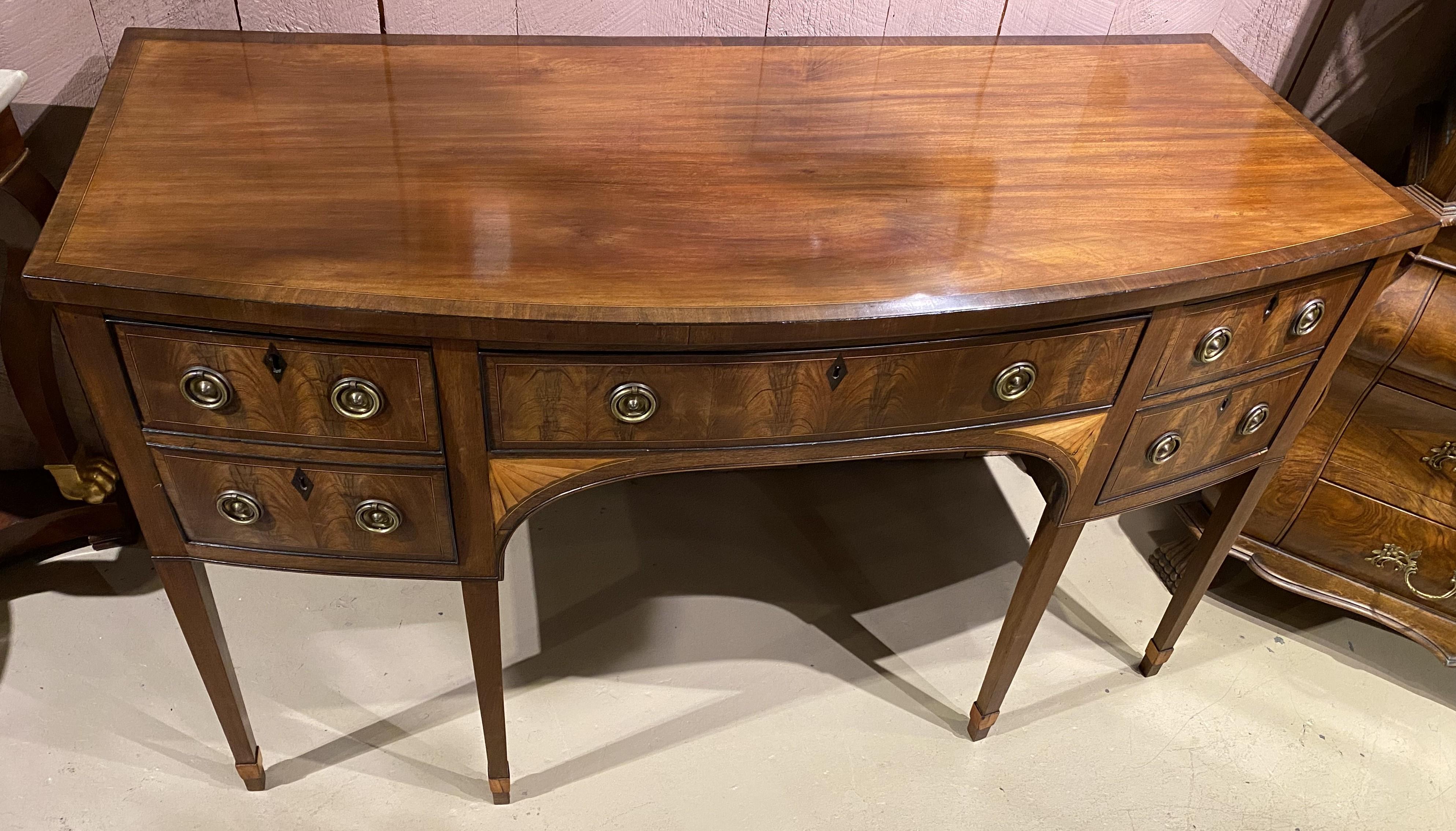 Fino aparador inglés georgiano de caoba con frente arqueado, tapa conformada con un borde de chapa de madera entrecruzada sobre el que se sitúa una caja con un cajón central con friso e inserto de fieltro verde para cubertería, flanqueado por un