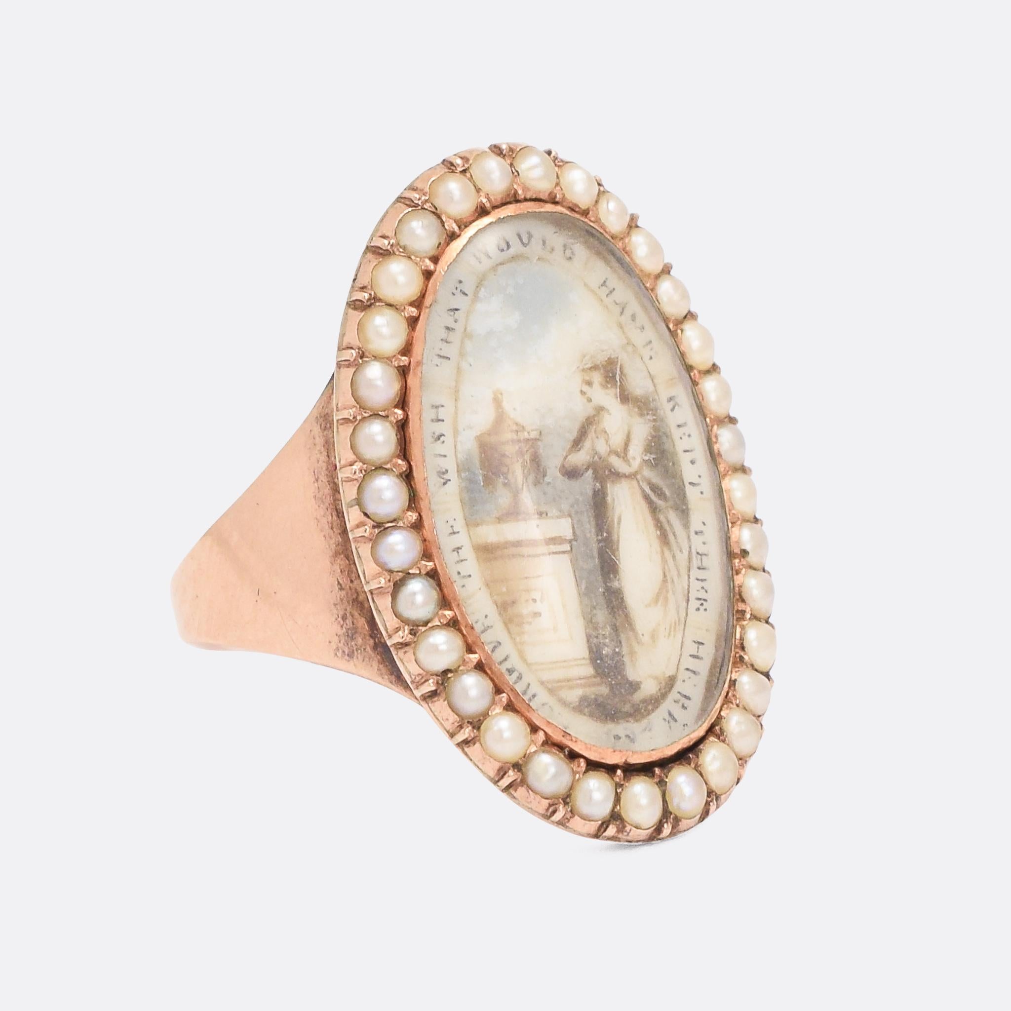 An incredible antique navette memorial ring with a finely painted oval panel set within a halo of seed pearls. The panel depicts a lady in mourning, stood by a plinth and urn, with the words 