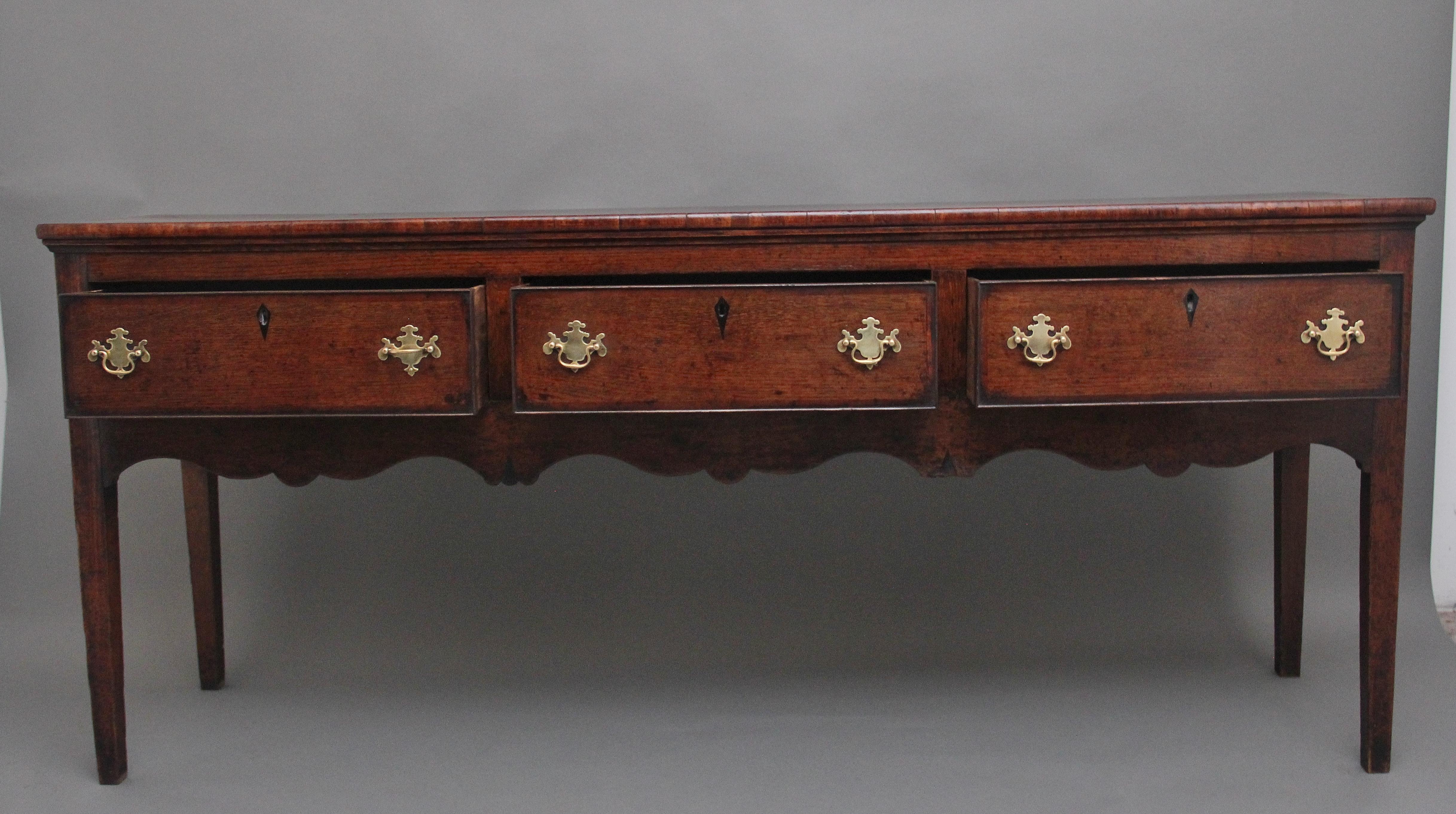 18th Century oak dresser base, having a lovely figured top above three deep drawers with brass plate handles, crossbanded on the drawer fronts, with a decorative shaped frieze below, panelled sides and supported on square legs.  In excellent