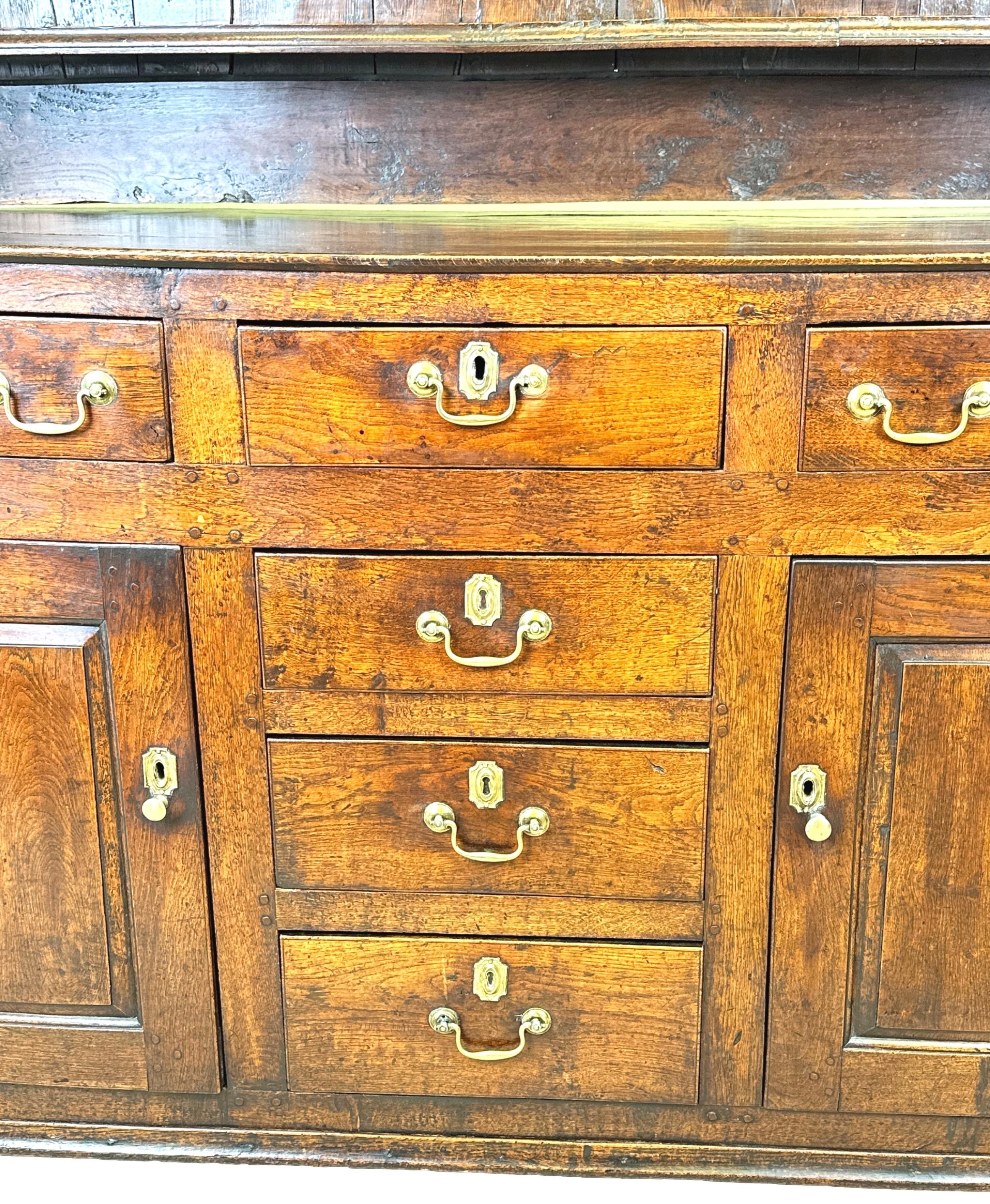 A Charming Mid 18th Century Georgian Oak Dresser, Of Superbly Untouched Rich Colour And Patina, Having Original Rack With Three Fixed Shelves And Panelled Back Flanked By Elegant Shaped Ends, Over Base With Six Drawers Retaining Original Brass Swan