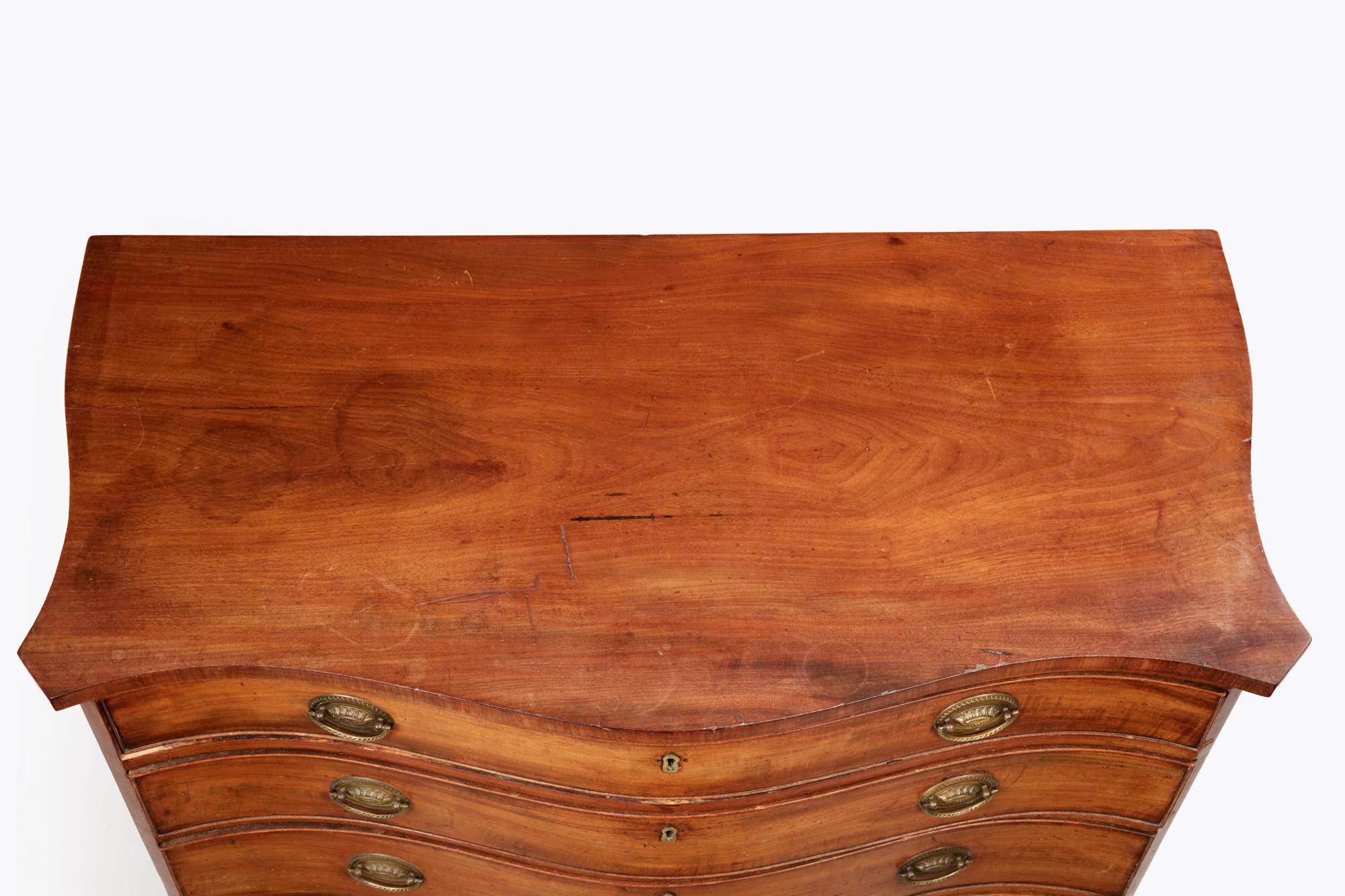 Mid-late 18th Century Georgian serpentine chest with brass locks and oval-shaped pulls on four graduated drawers raised on outswept bracket feet.