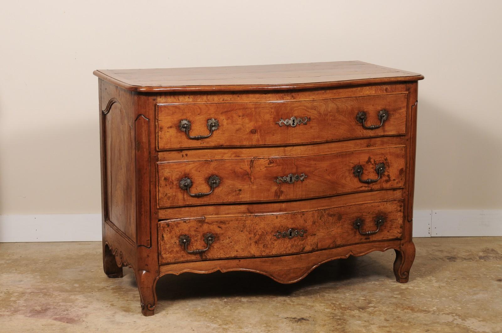 An 18th century Georgian Period walnut commode, of serpentine form. The top crossbanded and set above three drawers with applied pewter flower backplate handles, paneled sides, the lower parts with shaped aprons and supported upon carved cabriole