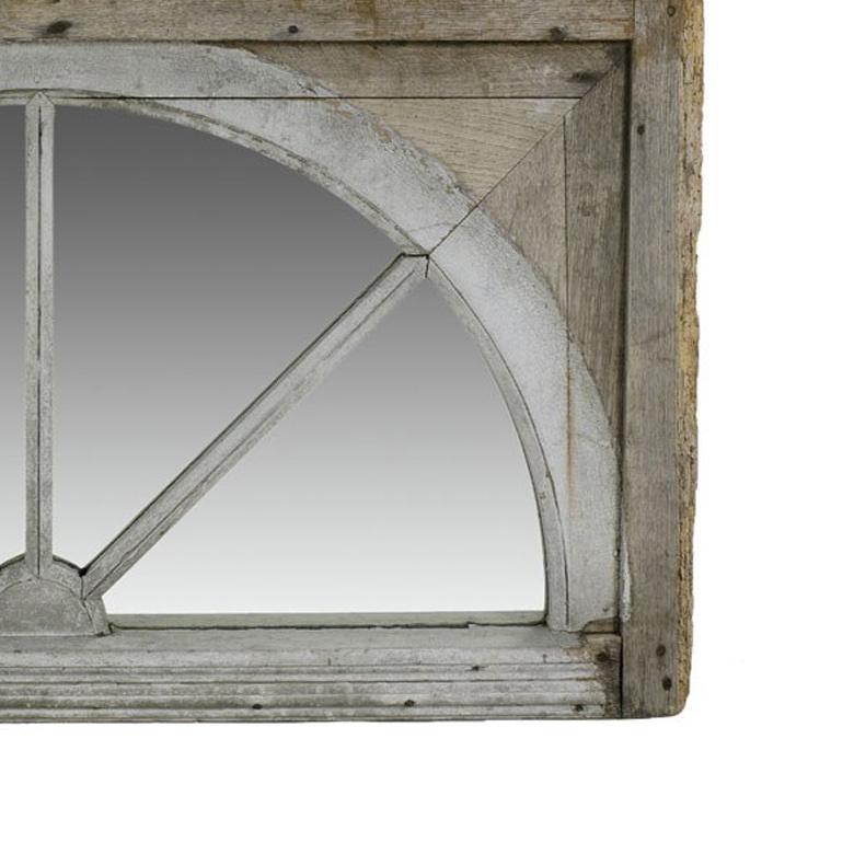 Rustic architectural overdoor mirror set in 18th-century English fan-shaped window pane. The piece started as a window on a household designed in the traditional Georgian style. Having since been converted into a mirror, the piece retains its