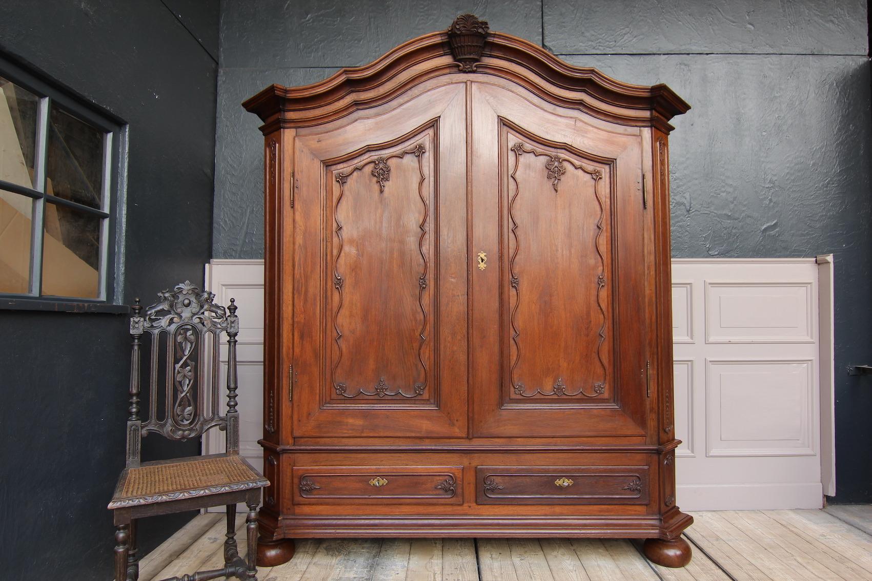 German baroque cabinet made of oak. Around 1780. Probably from the Aachen area.

Wax polished 2-door body standing on ball feet with bevelled corners and profiled base with 2 drawers. Floral carvings. 
Profiled broken cornice with a carved flower