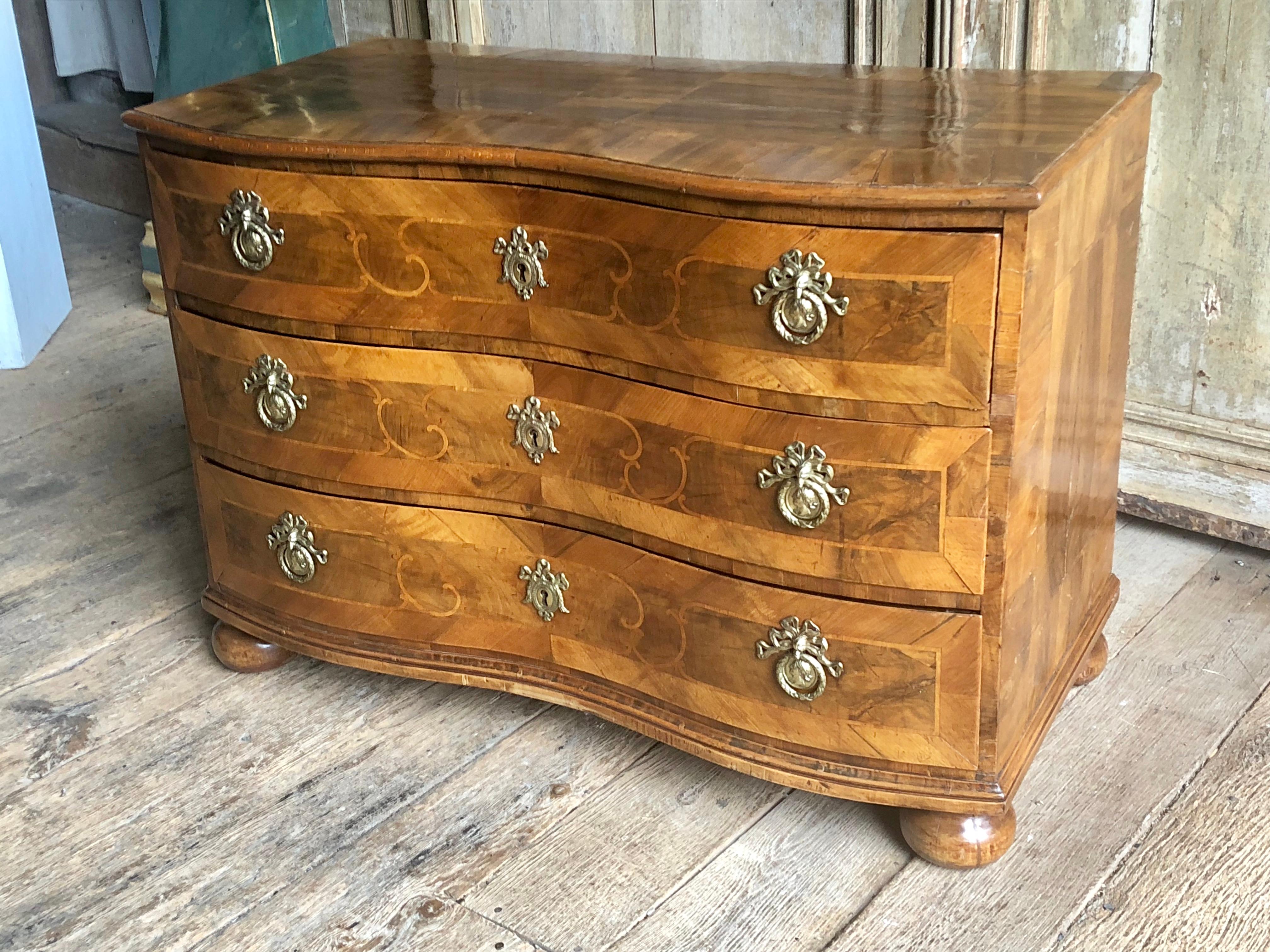 A fine 3-drawer Baroque German commode in walnut with inlaid fruitwood Marquetry decoration, the serpentine drawers retaining their original locks with key and brass drawer pulls and escutcheons, all on squat ball feet, mid-late 18th century.