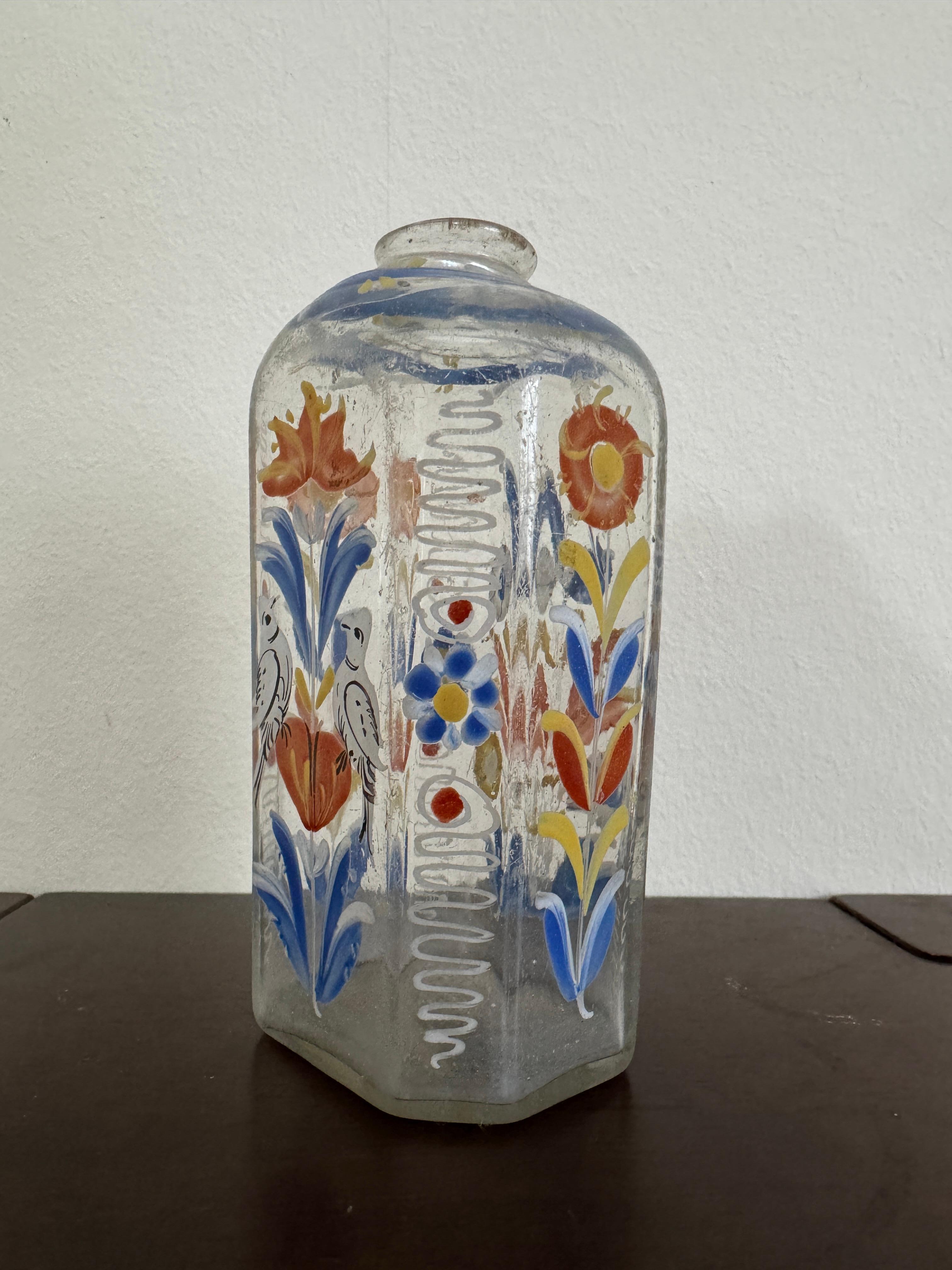Bottiglia di vetro trasparente del XVIII secolo, tedesca o forse boema. Forma ottagonale appiattita. Decorata a mano con fiori blu e arancioni e una coppia di uccelli bianchi sul davanti.

12,3cm / 4,75