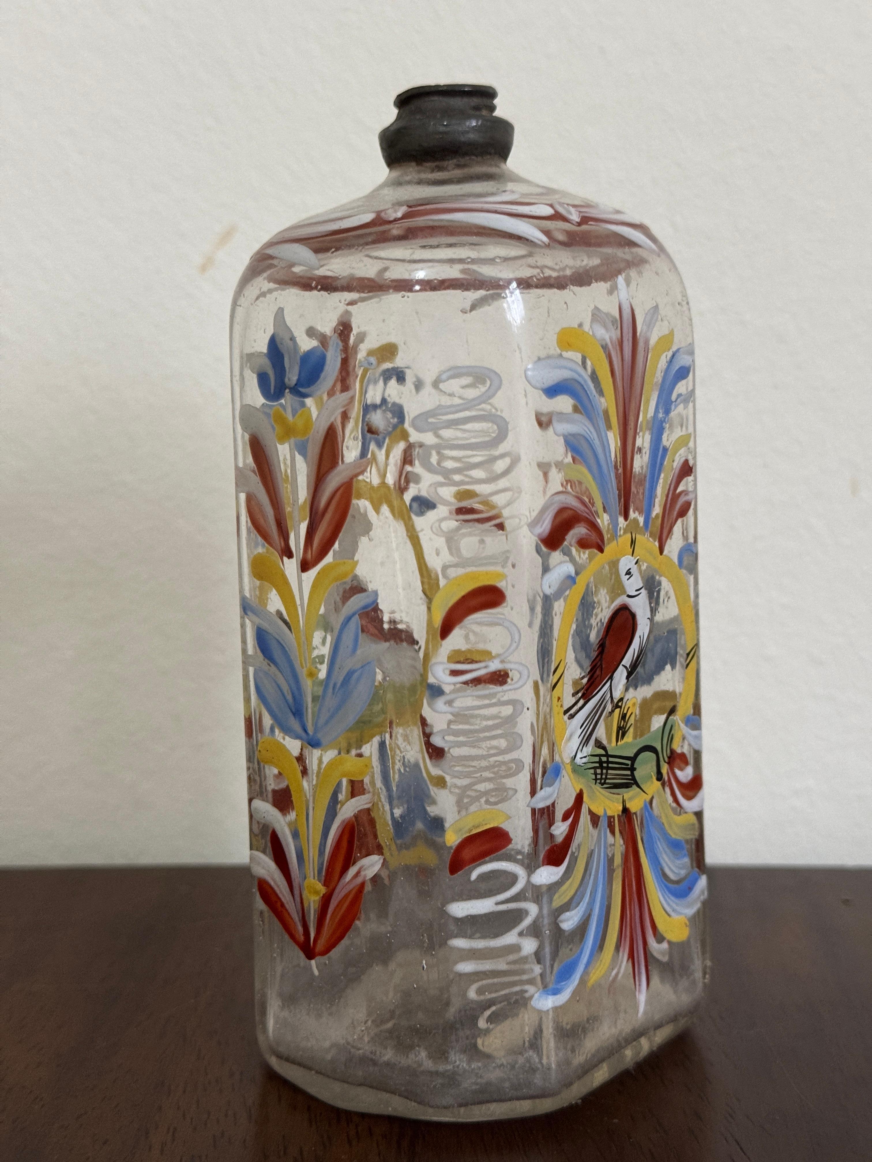 Bottiglia di vetro trasparente del XVIII secolo, tedesca o forse boema. Forma ottagonale appiattita. Decorata a mano con fiori blu, gialli e rossi sui lati e un uccello rosso e bianco appollaiato sulla parte anteriore e posteriore.

15cm / 5,75