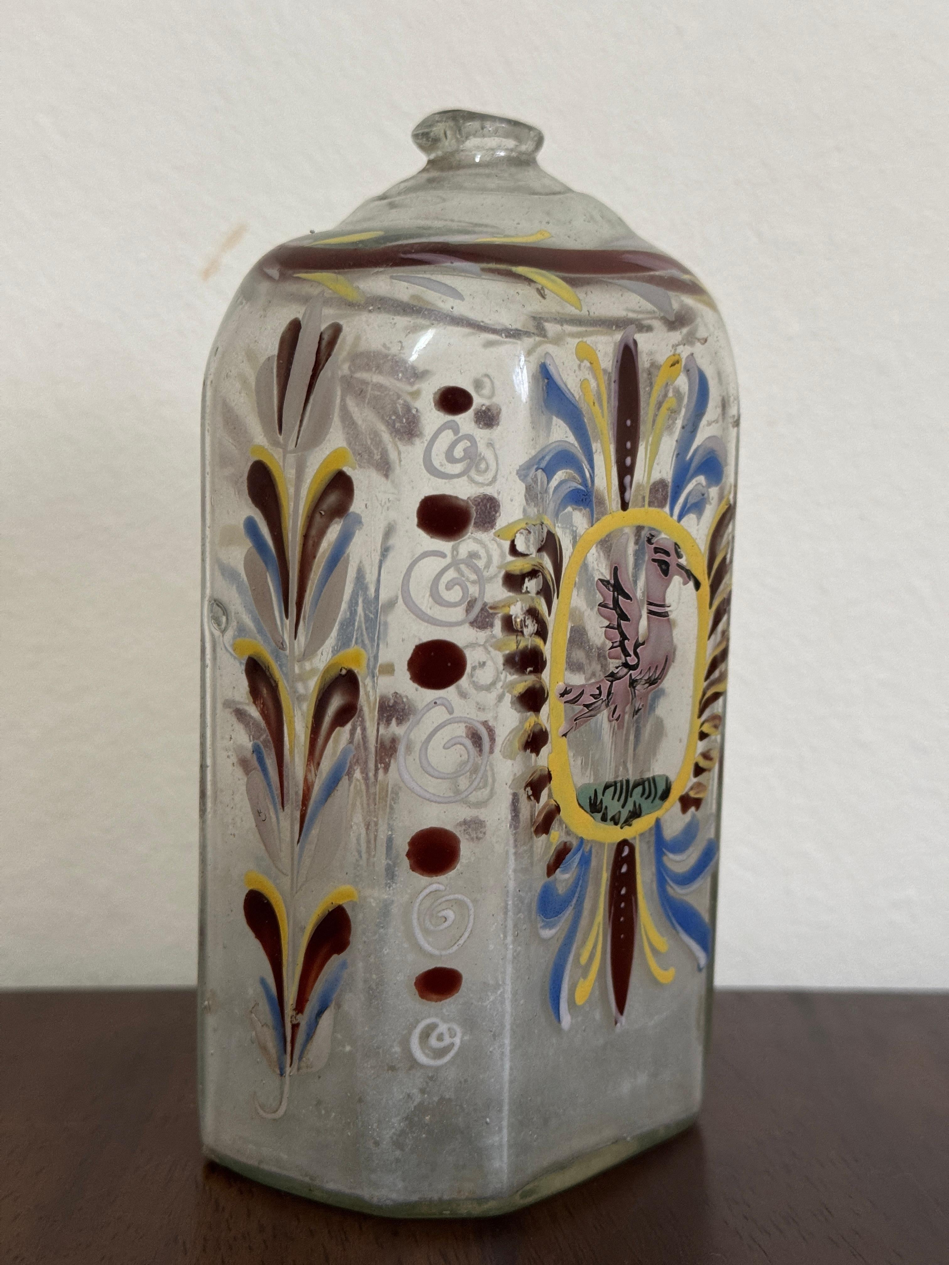 Bottiglia di vetro trasparente del XVIII secolo, tedesca o forse boema. Forma ottagonale appiattita. Decorato a mano con fiori blu, bianchi e marroni e un  uccello rosa sul davanti.

14cm / 5,5