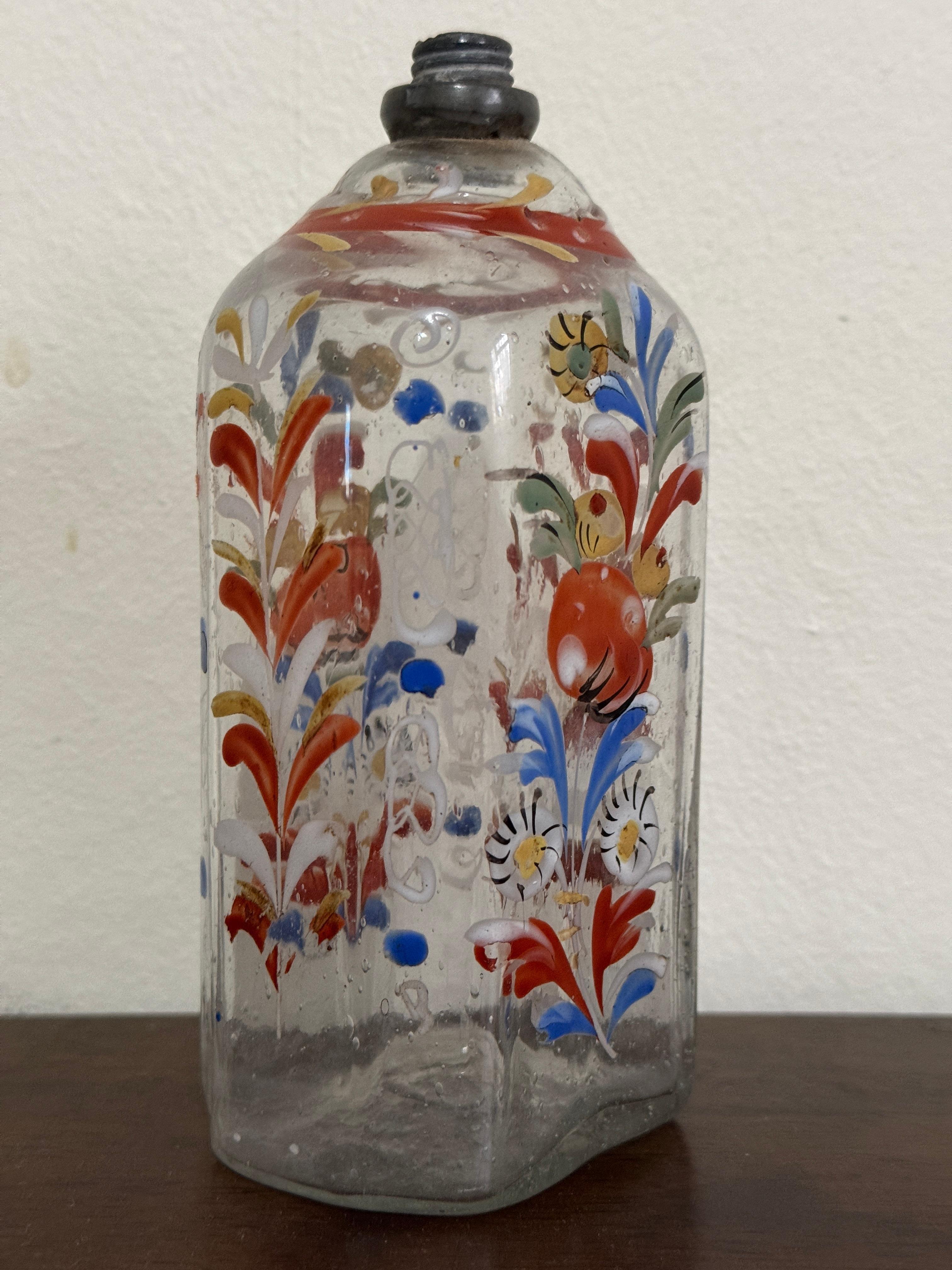 Bottiglia di vetro trasparente del XVIII secolo, tedesca o forse boema. Forma ottagonale appiattita. Decorato a mano con fiori blu, bianchi e arancioni.

14,5 cm di altezza