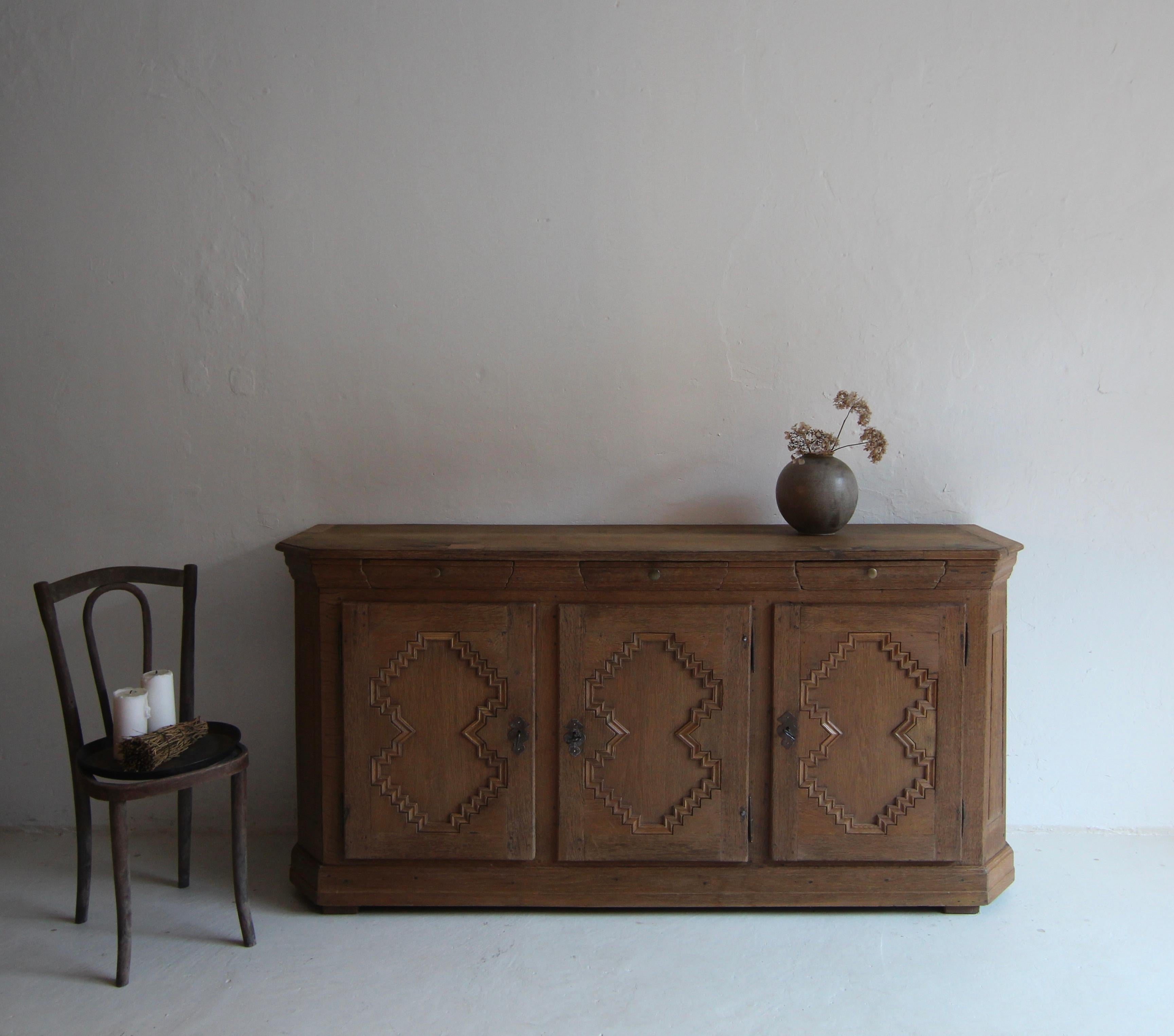 A late 18th century Baroque sideboard or milk cabinet. Probably from north-west German. Made of solid oak.

Beautiful charming piece with patina and character.

Solid three-door oak body with bevelled corners and slightly protruding profiled cornice