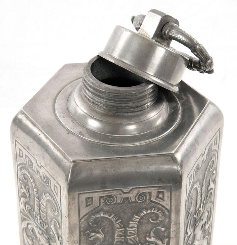 A German pewter six-sided canister with a twisting lid fitted with a handle in the form of dragon heads, above a body with conforming panel decoration: curling horns emerge from crown, which resting on an armoured mask that sits above an unadorned