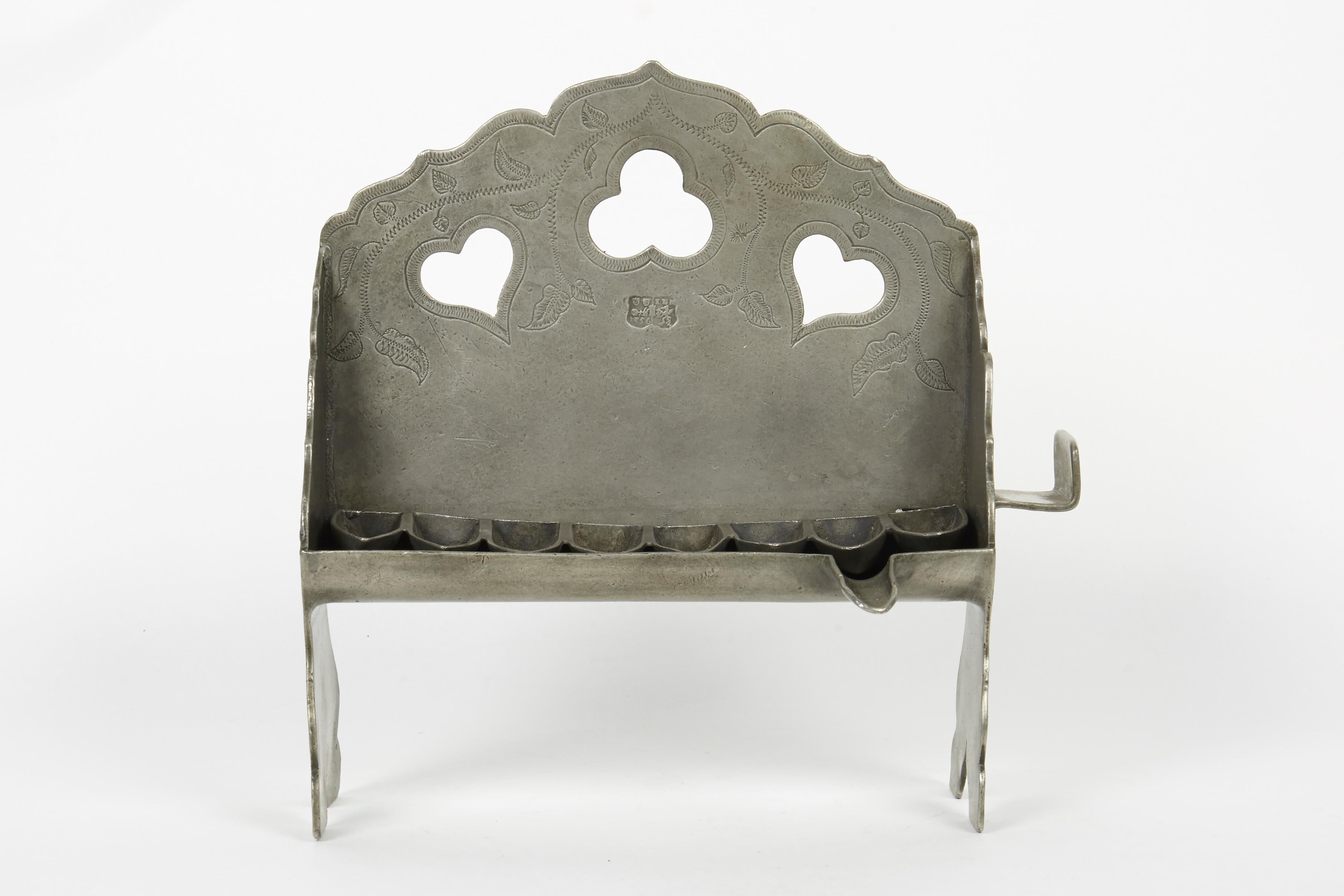Pewter Hanukkah Lamp, Germany, mid-18th century
The cartouche-form backplate is pierced with heart-shaped holes, engraved with stem and leaves, and fitted with a row of eight oil pans.
Marked with German pewter hallmarks.
