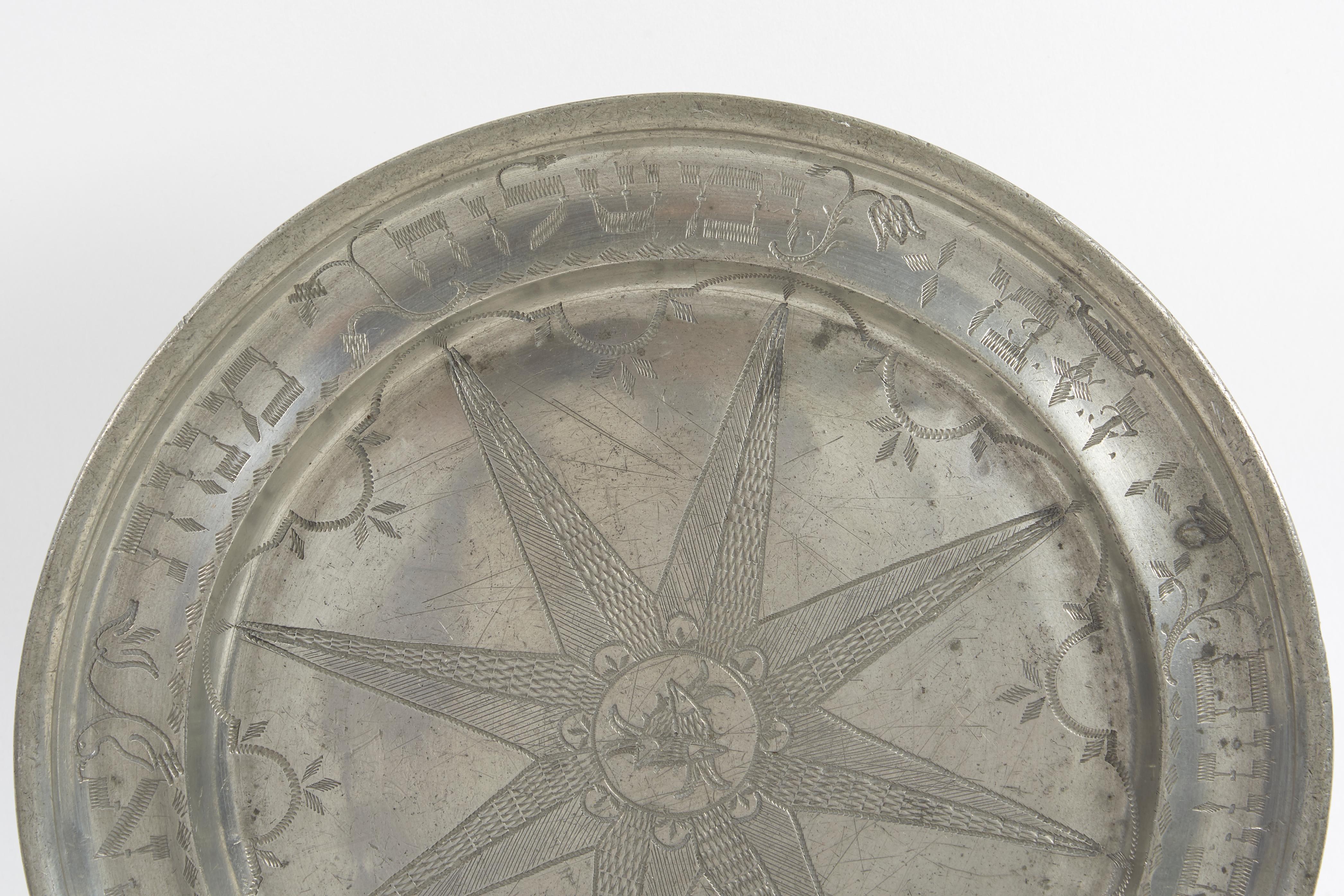 Pewter Purim dish, Germany, late 18th century.
The outer rim has wriggle-work engraving stating “and of sending portions one to another and gifts to the poor” (Esther 9:22). Interspersed between some of the words are depictions of foliage and