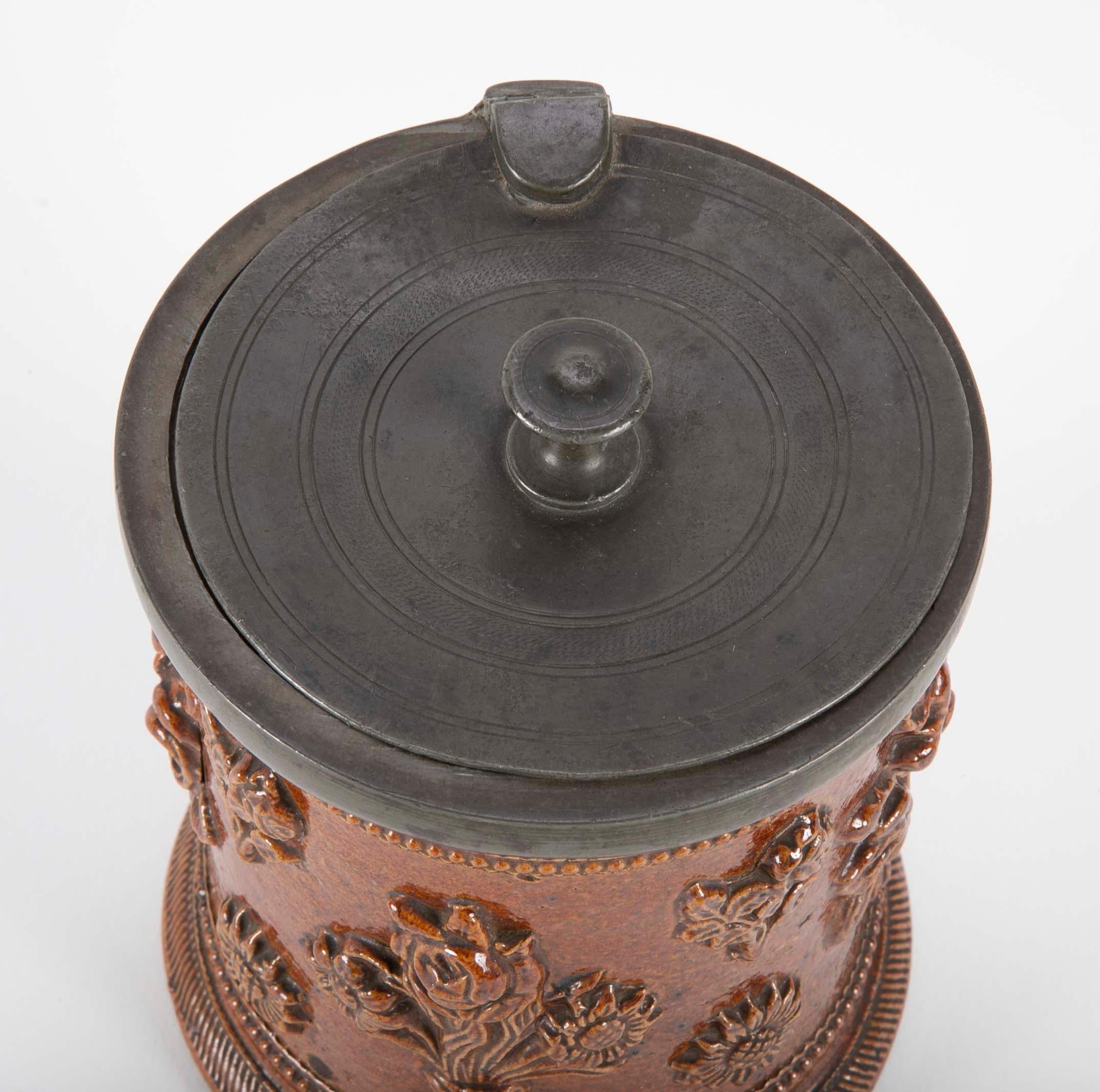 A fine example of a German Baroque tobacco jar with original pewter lid. The rich ocher salt glaze decorated with raised floral motifs. A handsome addition for the collector of pipes and tobacco accessories. Or as a beautiful and unique decorative