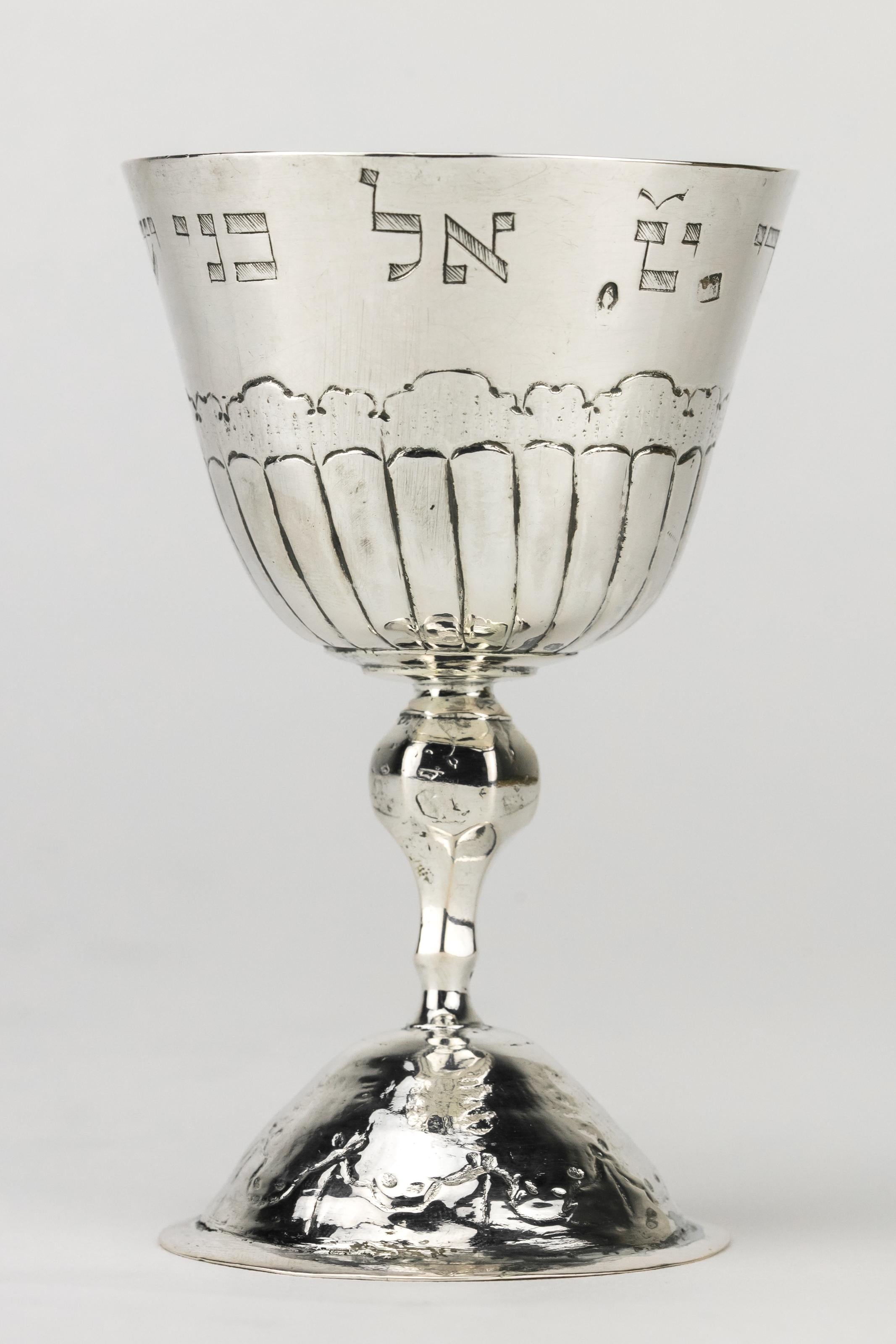 Silberner Kiddusch-Kelch, Hieronymus Mittnacht, Augsburg, Deutschland, 1763-1765.
Tulpenförmige Schale im klassischen Stil mit ziseliertem Wellenmotiv und facettiertem Balusterschaft auf kreisförmigem Sockel mit koordinierter Ziselierung. Am Rand
