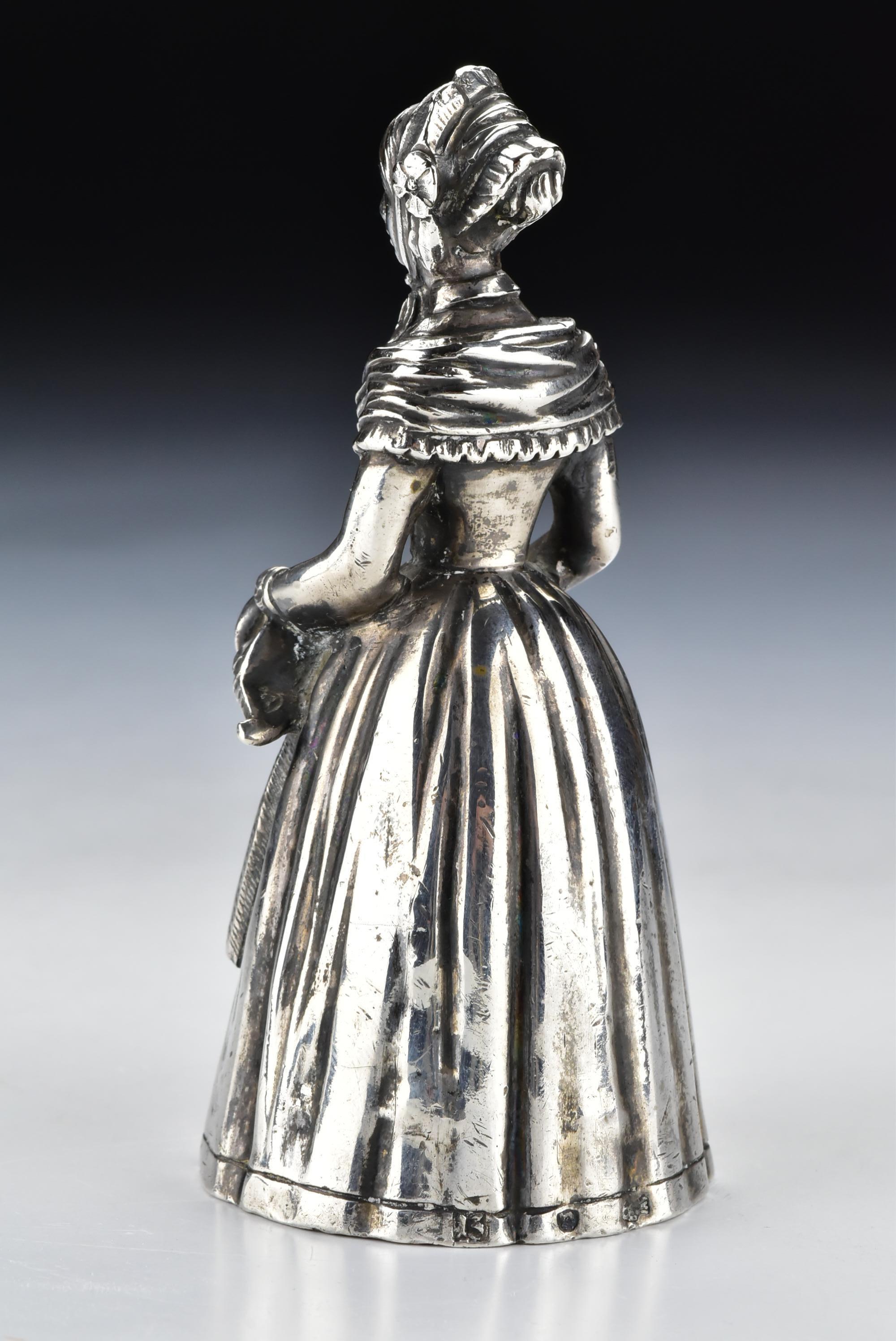 German silver dinner bell in the form of a woman, hallmarked along the bottom edge of her dress. 

Age: Kassel city mark dating from the late 18th century

Size: Approximately 4 + 1/8 inches tall by 2 inches at it's widest point, approximately