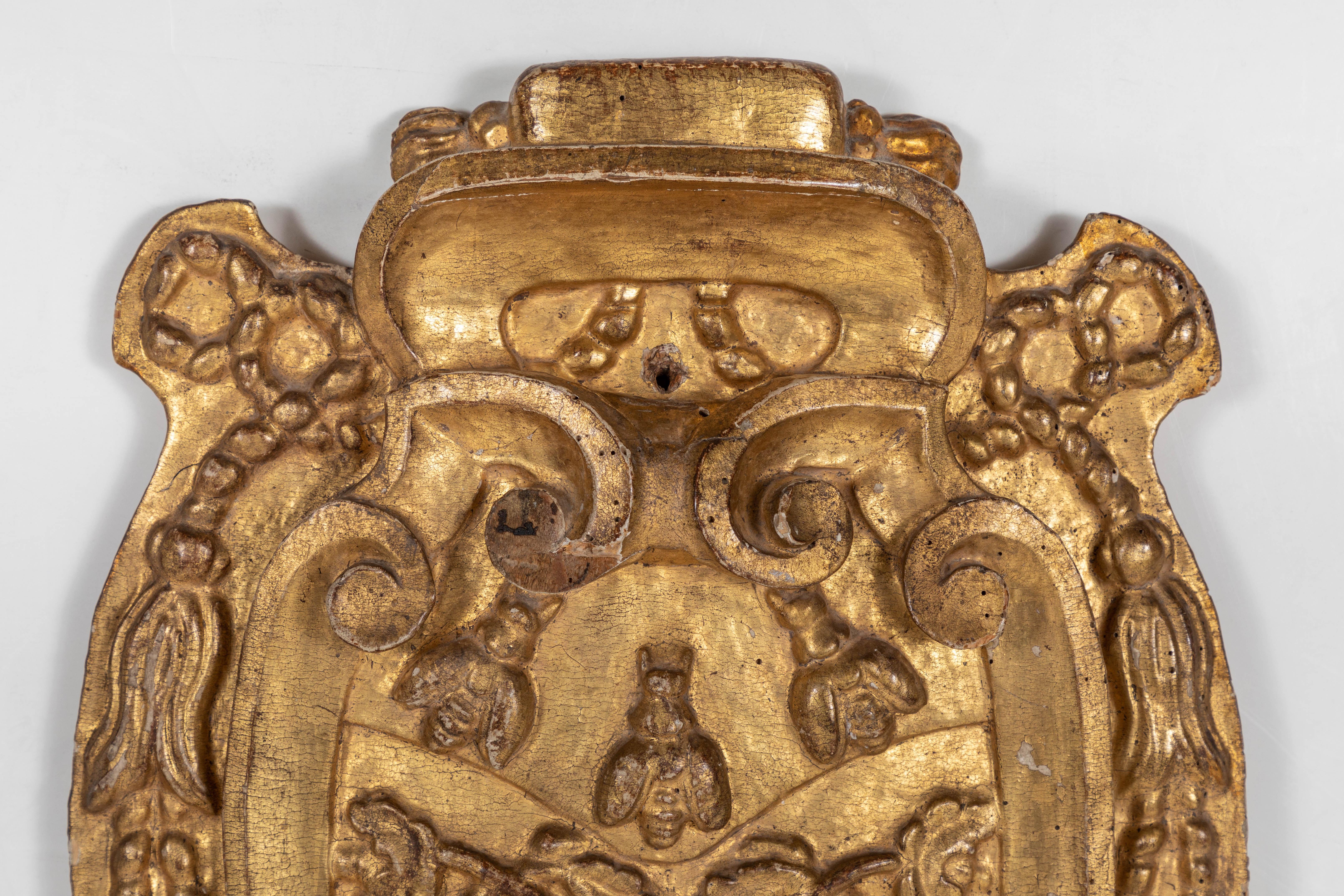Relief carved, gessoed and 22-karat gold gilded, Italian bishop's crest featuring three bees amidst foliate scrolls, drapery swags, and tassles.