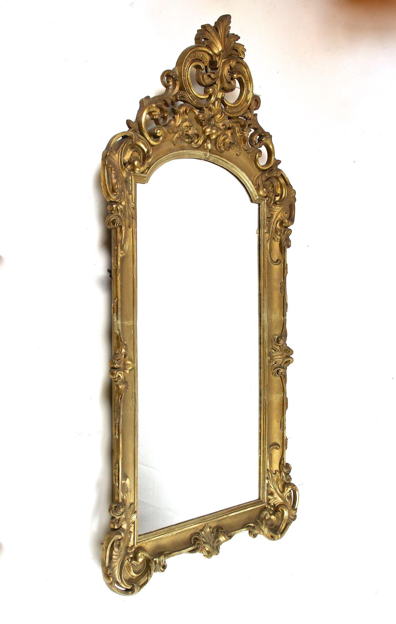 Extraordinary 18th century gilt wall mirror from the late baroque period in Austria around 1780. This artfully handcarved frame shows different gilt techniques (gold leaf/ composition gold/ bronzed) and is adorned by elaborately carved corners