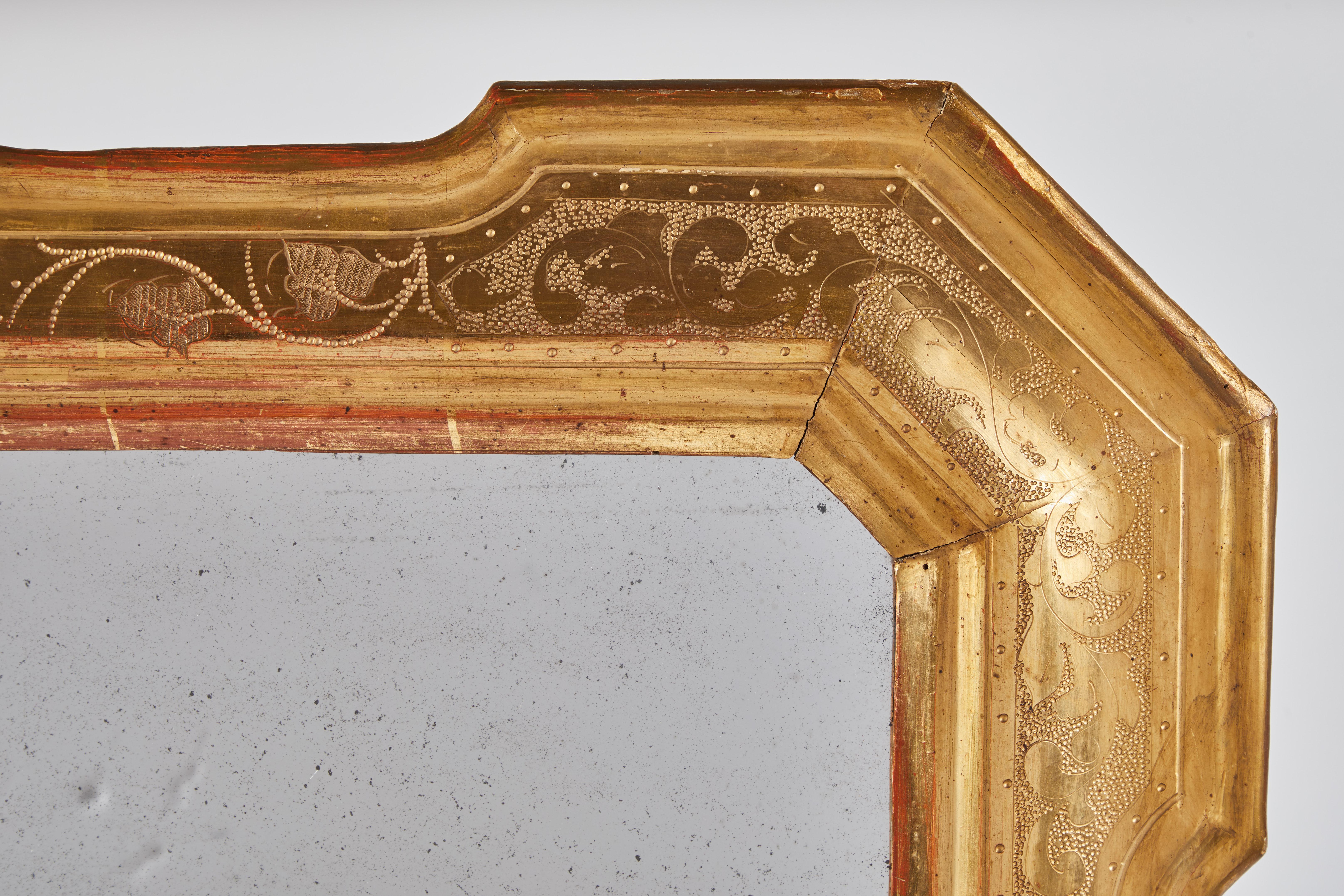 An 18th century mirror with hammered detailing from Lombardy. Petite rectangular frame with angles corners. Very sweet floral detailing hammered into the gilt frame.