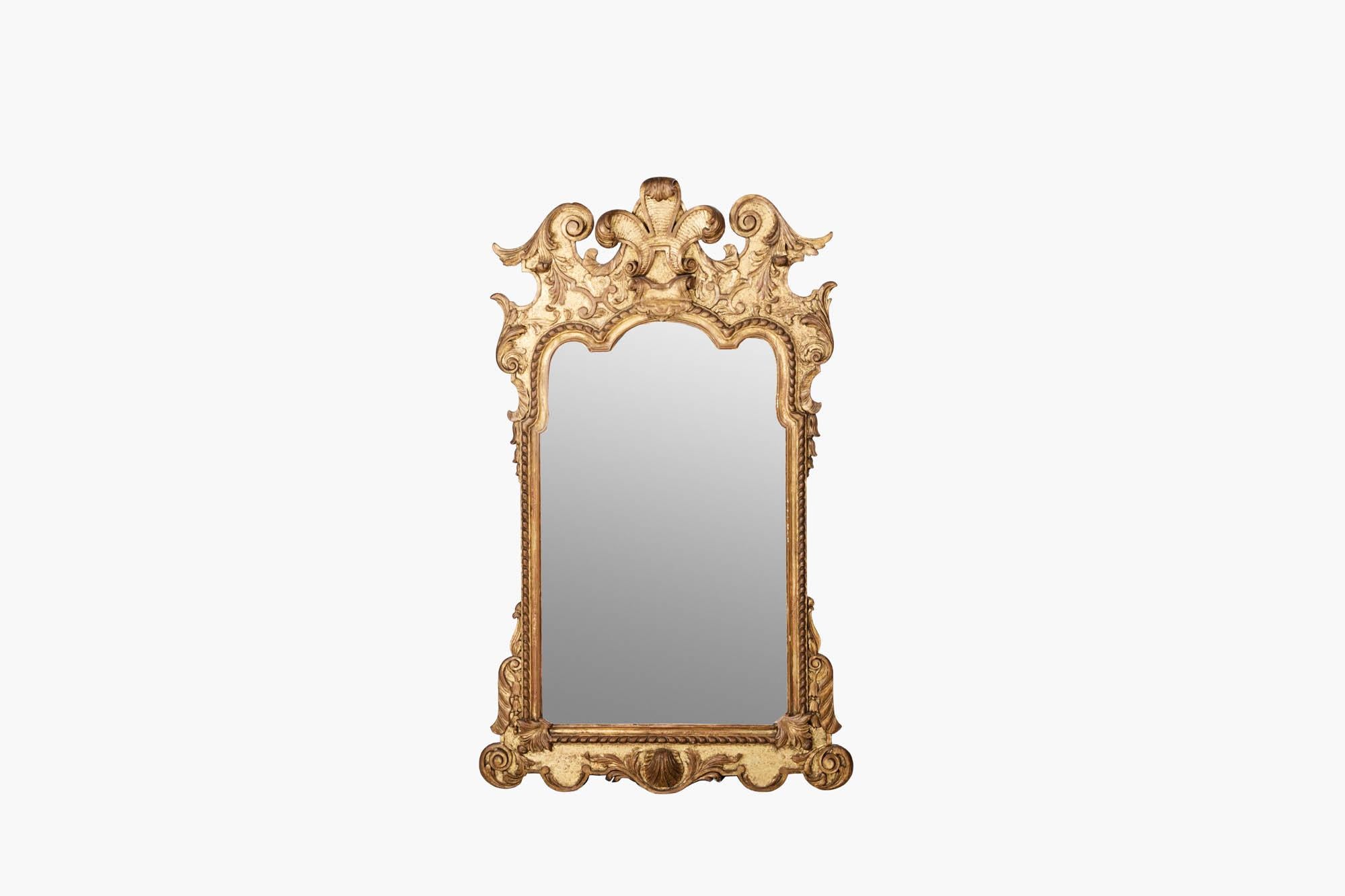18th century gilt mirror with arched plate in the manner of Belcher. Hightly decorated throughout, the frame displays scrolled foliate detailing, bell drop flowers to the left and right sides, Prince of Wales feathers to the top, and seashell motif