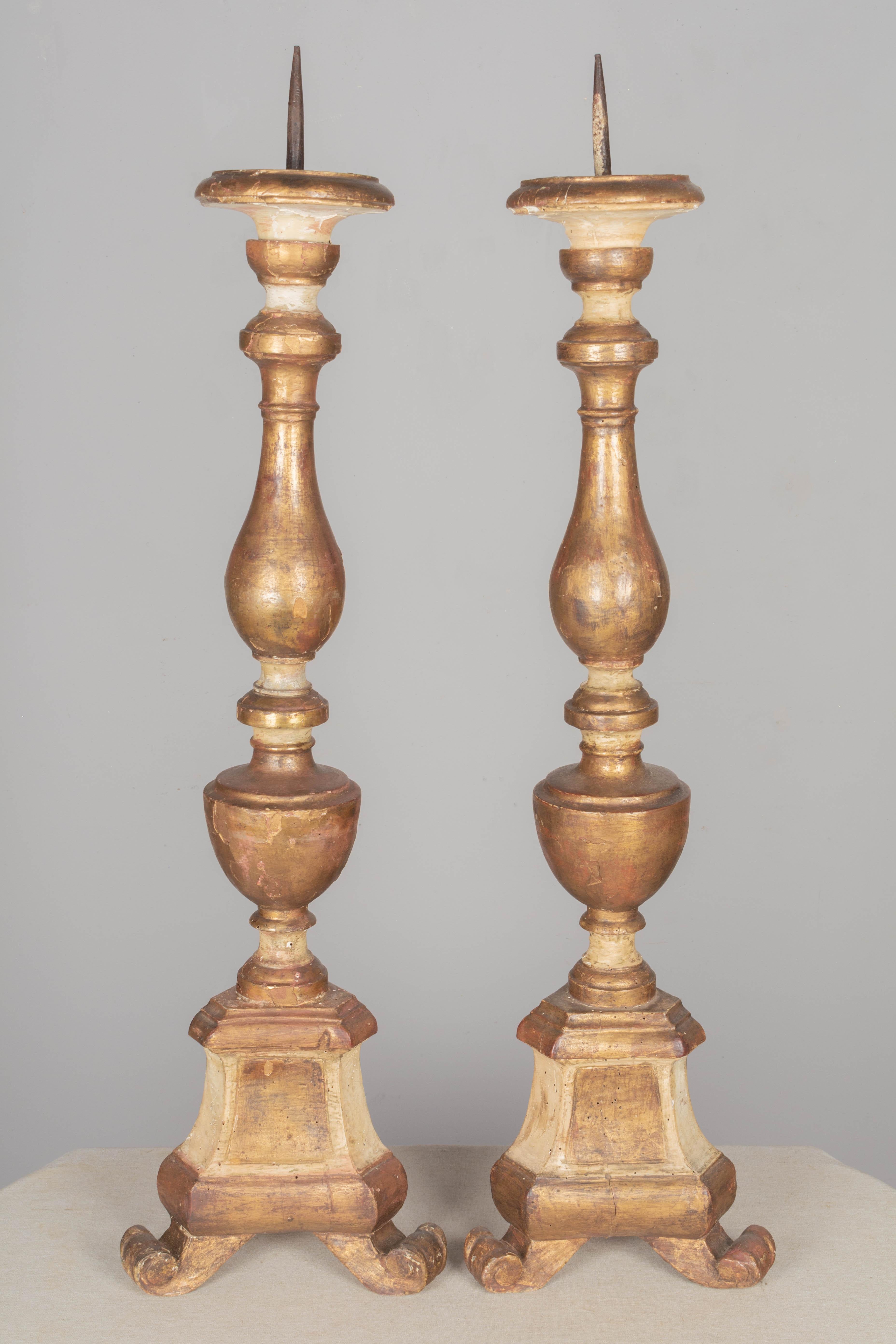 A pair of 19th century Italian giltwood altar candlesticks. Tall columns on a trefoil base. Zinc prickets. Distressed gilt finish. Heavy gilt losses and touch-ups. 
Measures: 11