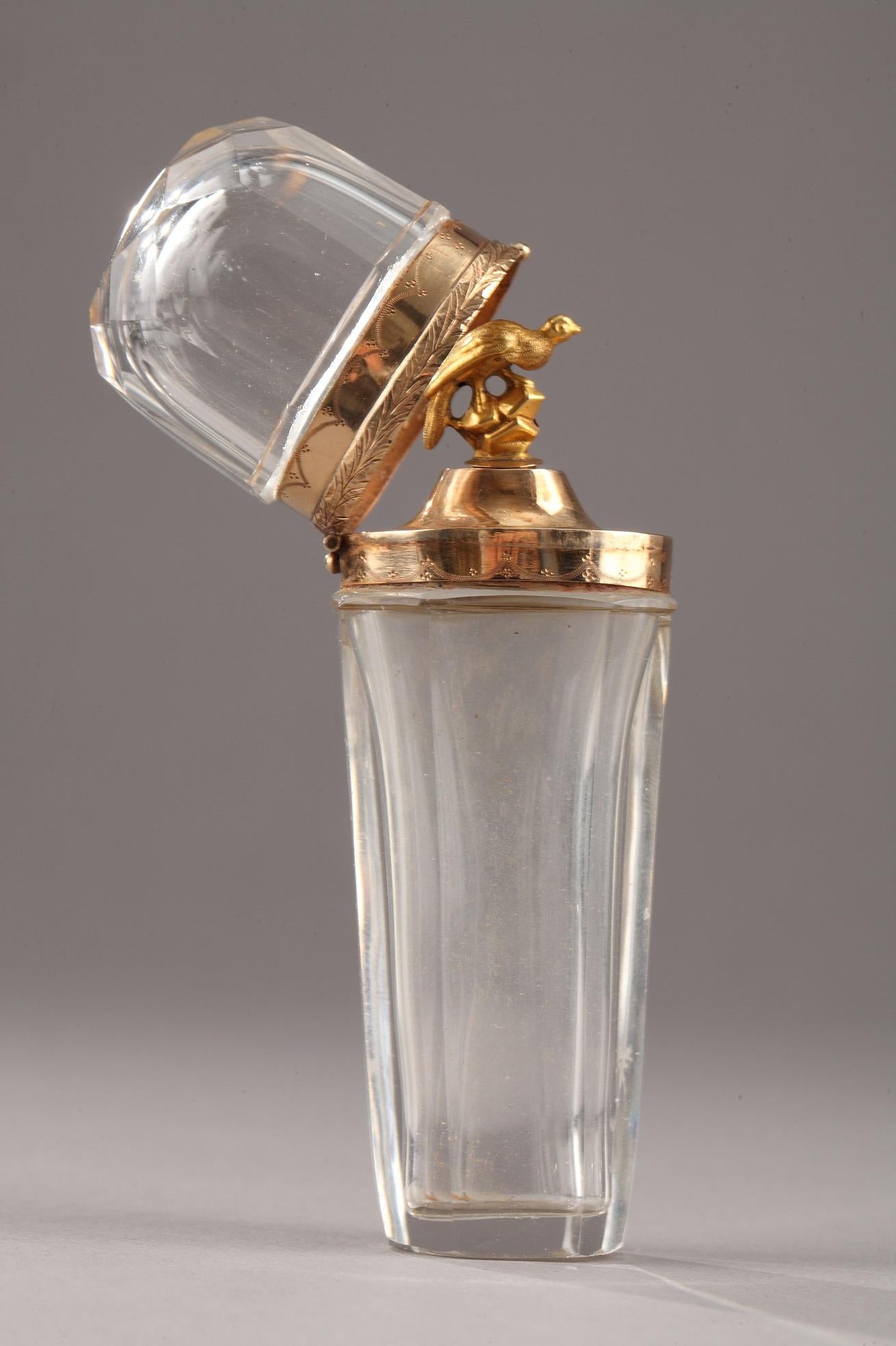 Conical shaped bottle in faceted crystal and gold setting. The conical bottle set in a gold mount opens with a hinge. Inside, the cap has a gripping shaped bird. Once the cap is closed, it forms a 