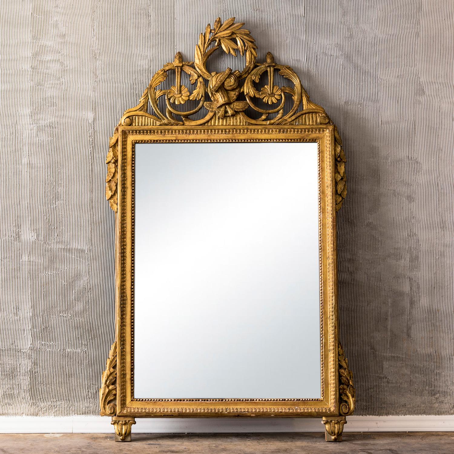 An antique rectangular mirror inscribed in a Pinewood, gilded frame adorned with water leaves and pearl friezes, in good condition. The mirror is consisting its original mirror glass. The Pediment is decorated with a central trophy in the center,