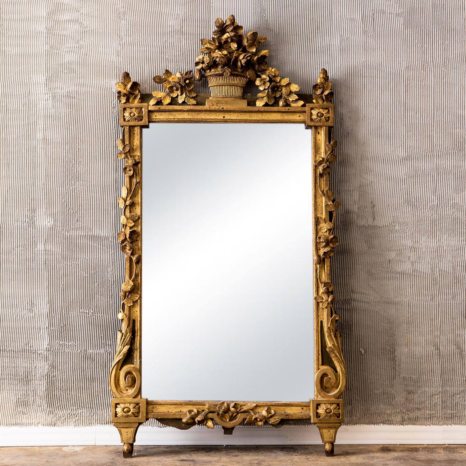 An antique rectangular mirror inscribed in a Pinewwood frame, gilded, the pediment formed by an openwork flower basket spilling sinuous garlands of flowers and foliage on either side, in good condition. The mirror is consisting its original mirror