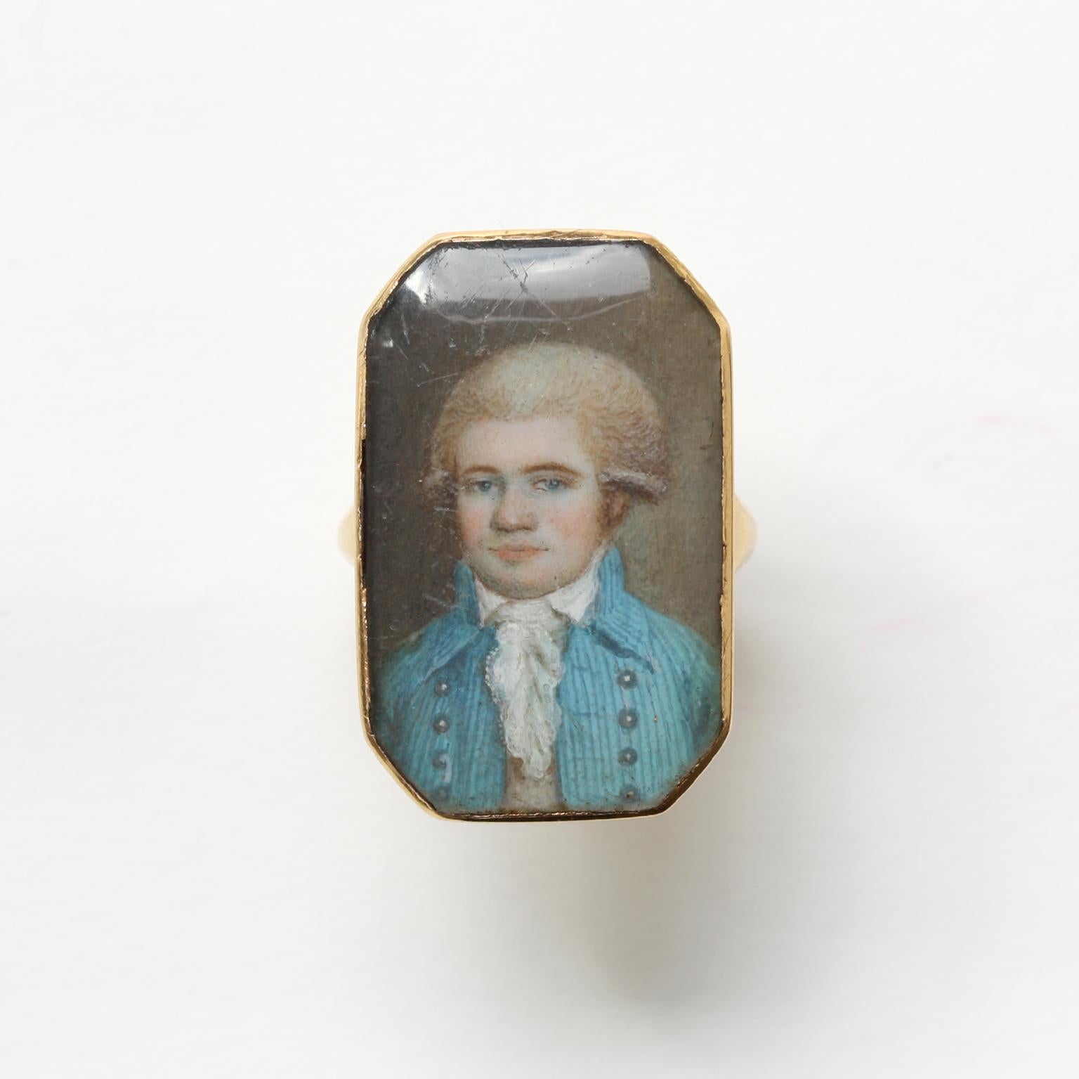 An 18th century octagonal gold ring featuring a glassed portrait of a young man wearing a wig and a pretty blue and white striped jacket, circa 1790, English or France.

ring size: 17+ mm / 6 ¾ US
weight: 5.74 grams
dimensions portrait: 2.6 x 2.1 cm