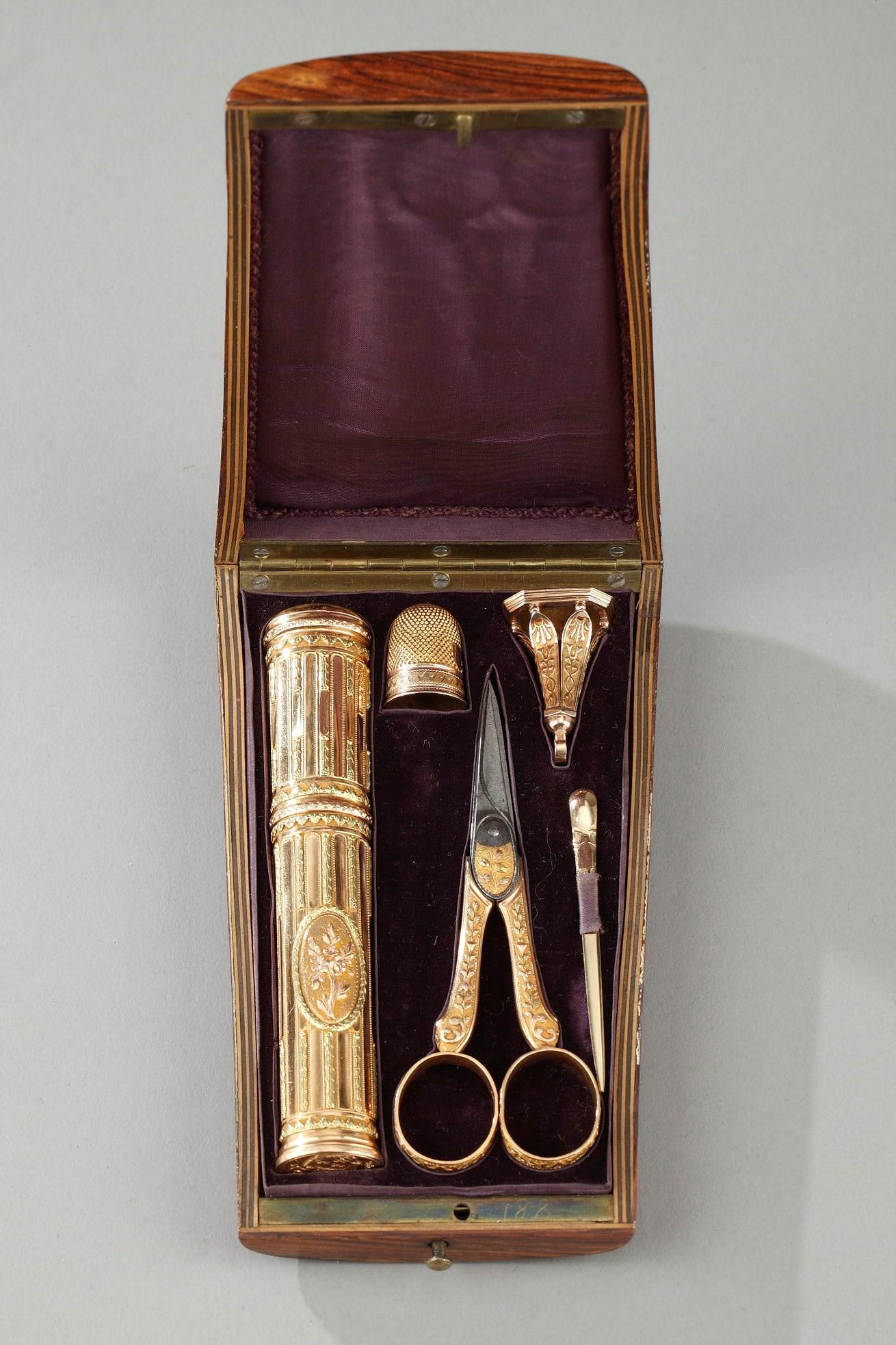 A 18th century set presented in trapezoidal case made of light wood and inlaid with marquetry. The vanity case includes a gold wax case decorated with flutes, a dice and a wool needle, a gold seal and a pair of gold and steel scissors. The Louis XVI