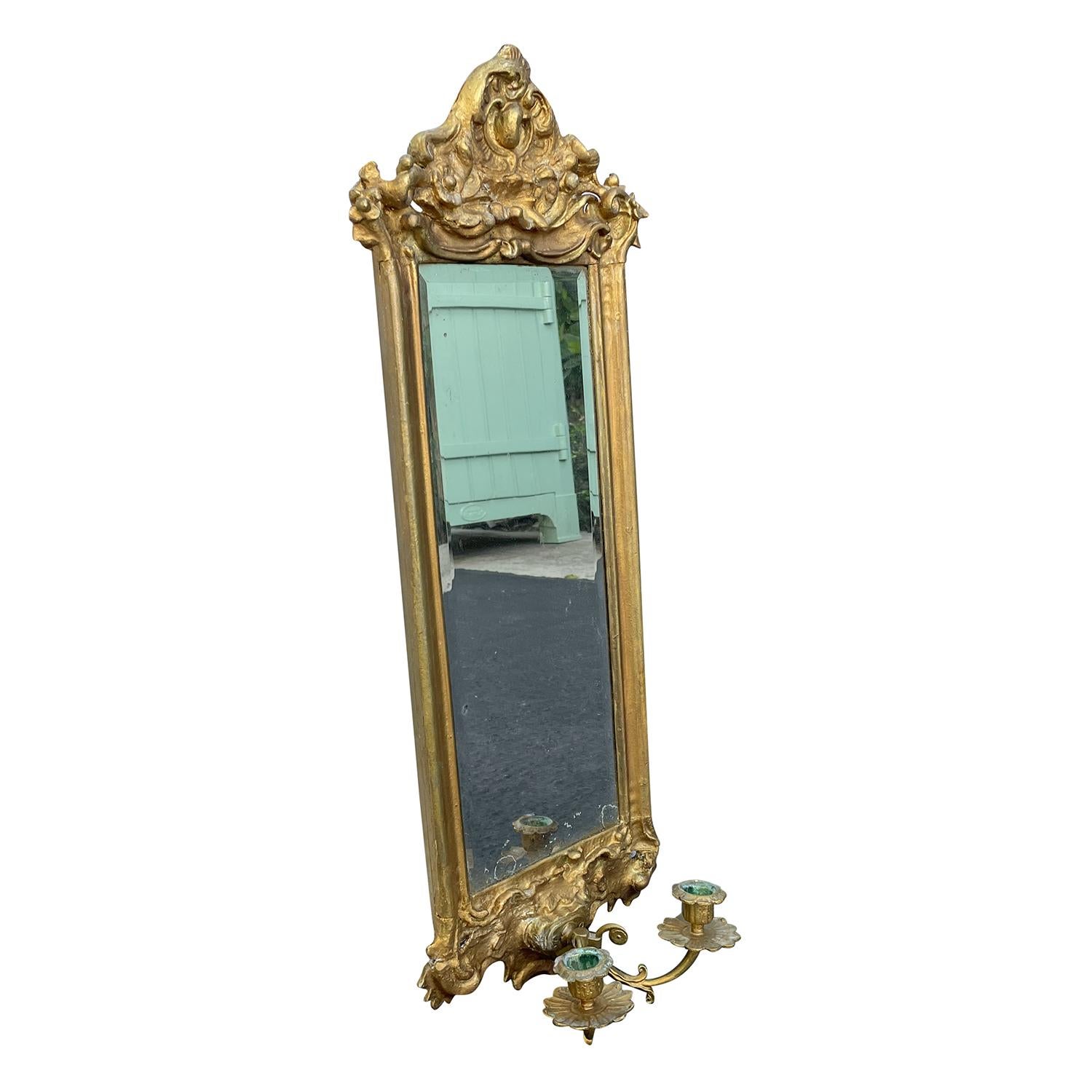 A gold, antique Swedish Gustavian pair of wall mirrors made of hand crafted gilded wood with its original mirrored glass, in good condition. The Scandinavian wall décor pieces are composed with two candle holders, sticks enhanced by detailed wood