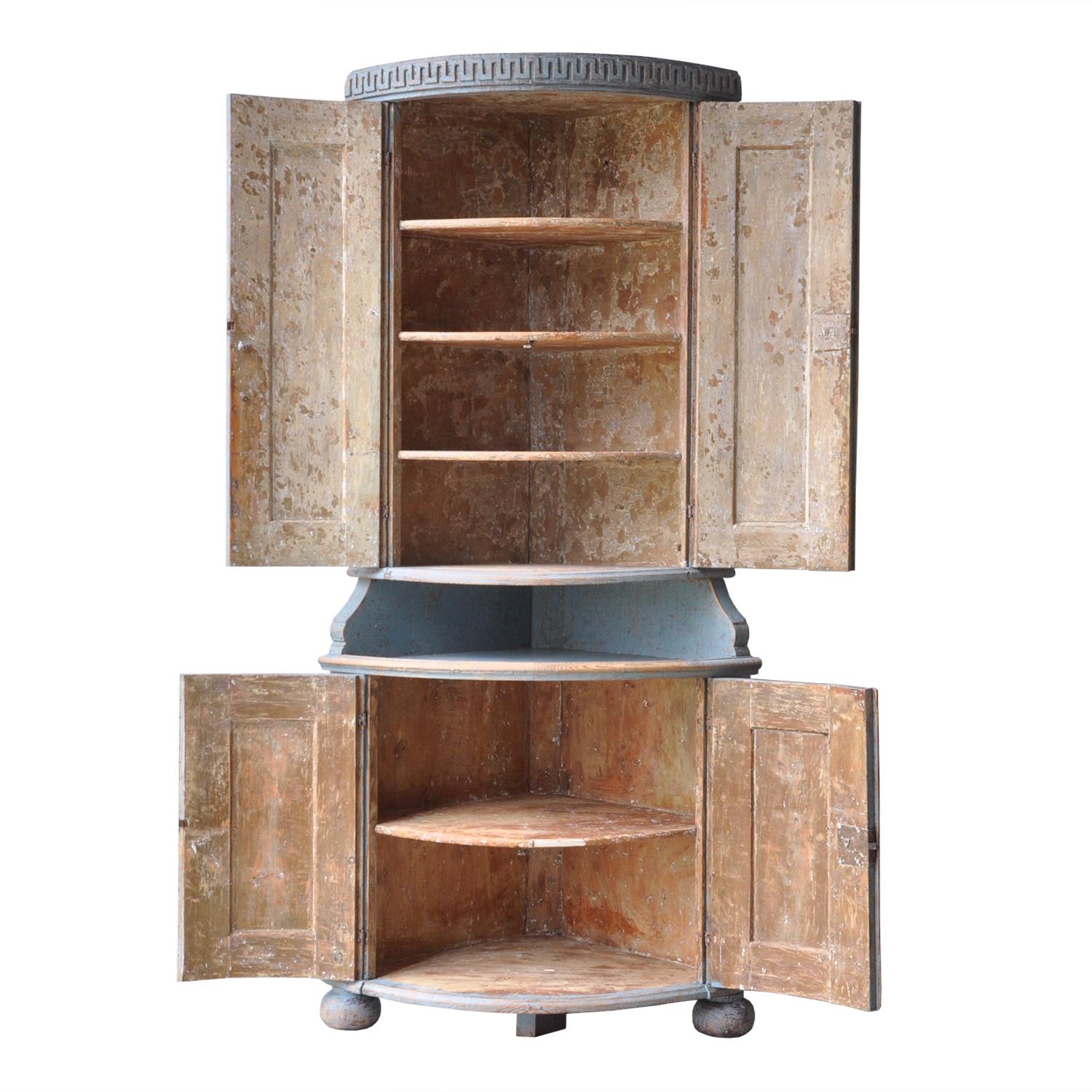 This curved front Gustavian corner cabinet dates from the 18th century. It features two curved doors at the top, opening to shelves, and a further two curved doors below also opening to shelves.
Between the two sets of doors is a curved open shelf.