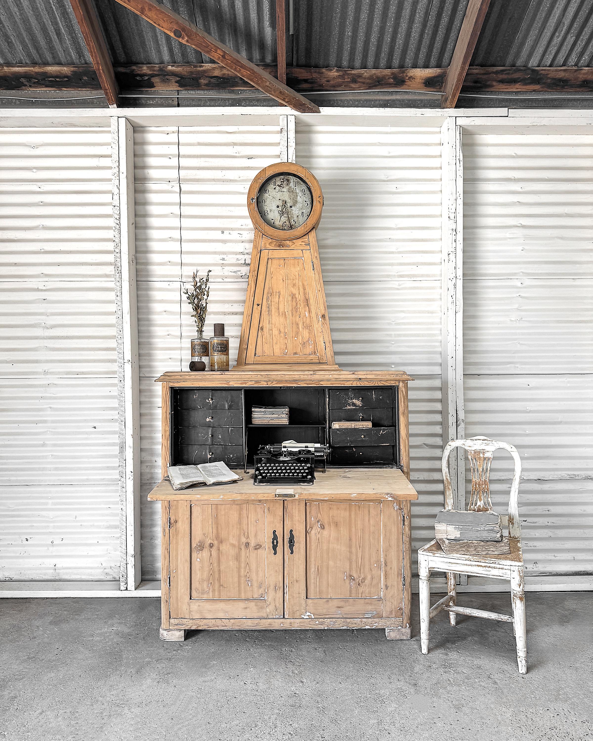 Rare exemple de design suédois multifonctionnel, ce sekretär med ur (secrétaire avec horloge) combine les deux meubles les plus importants d'une maison du XVIIIe siècle : l'horloge Mora et le bureau. Fabriquée en pin et reflétant l'élégance discrète