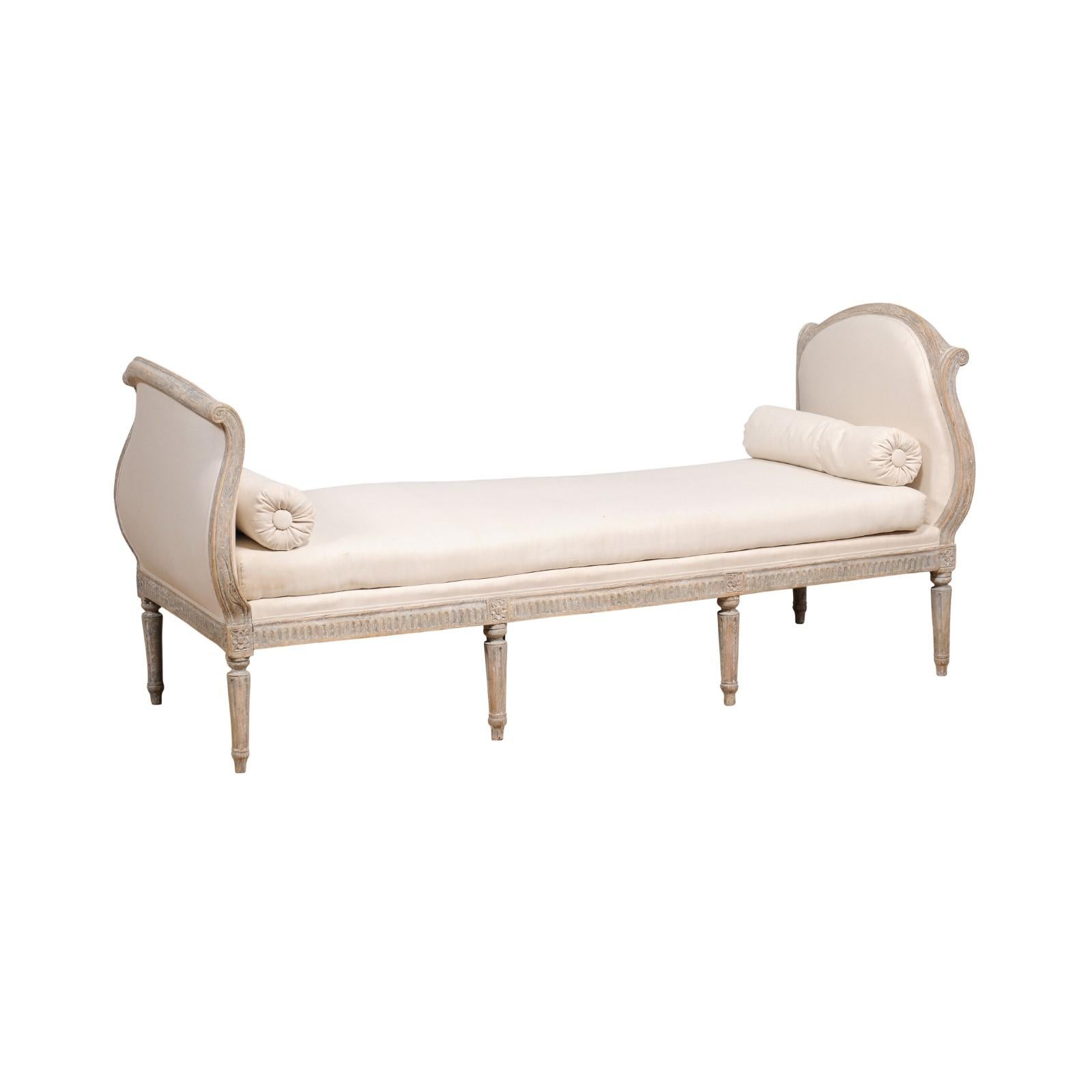 A Swedish Gustavian period grey painted daybed from the 18th century with out-scrolling sides, fluted apron and legs and carved rosettes. Step into an ambiance of timeless elegance with this 18th-century Swedish Gustavian daybed. Painted in a