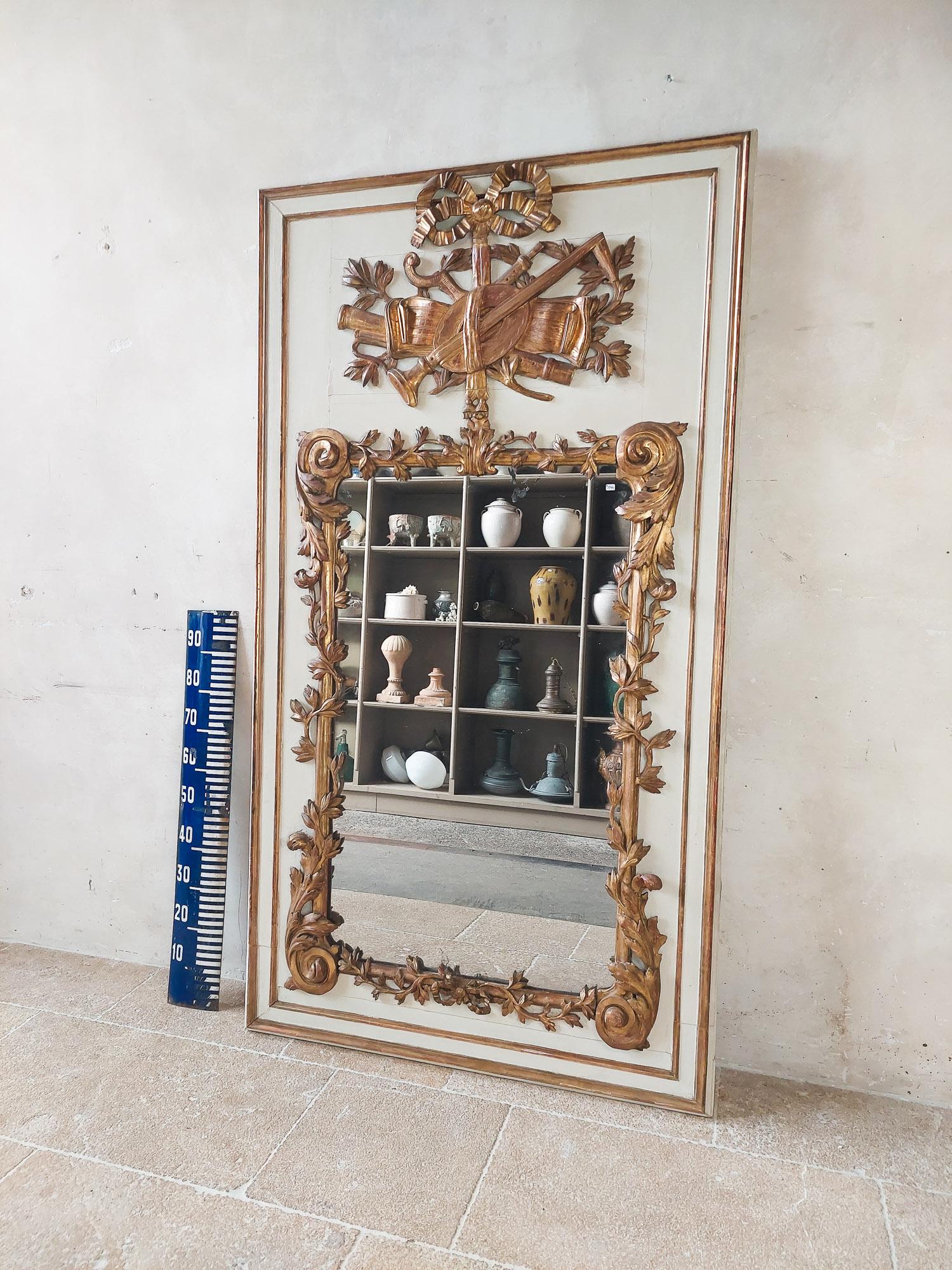 French 18th century giltwood trumeau mirror. Antique hand-carved basswood frame with white patina and gilded ornaments that fall in style in the transition of Louis the 15th and 16th.

The middle ornament depicting various musical instruments in