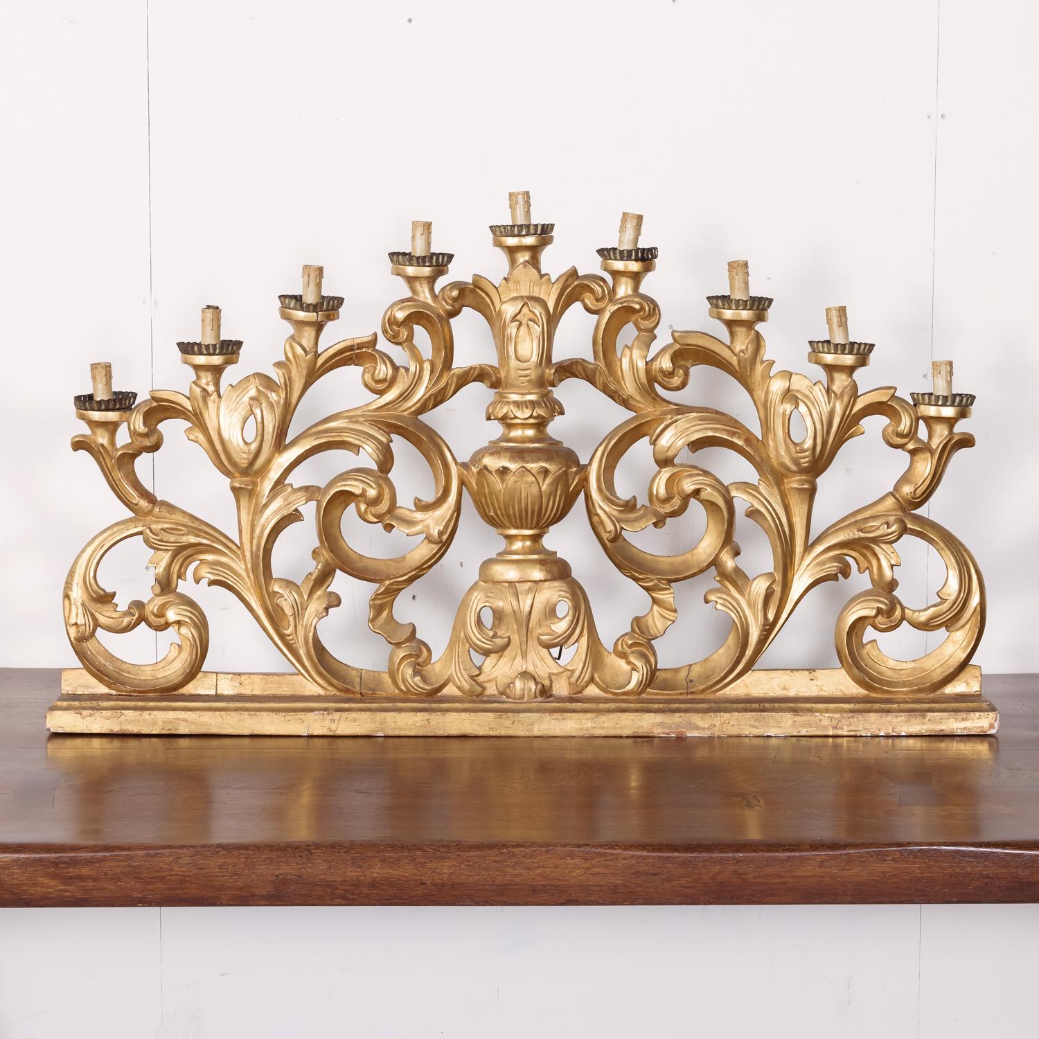 A spectacular 18th century hand carved Italian Baroque giltwood altar candelabra, circa 1780s. This large nine-light candelabra lamp features an opulent pierced giltwood design with a richly carved center urn flanked by elaborate scrolls and foliate