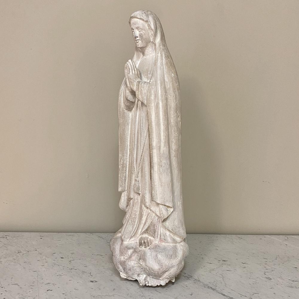 18th century hand carved wooden statue of Madonna is a splendid work of devotion, with the Virgin Mary in a prayerful pose dressed in robes symbolic of her piety. The carvings are accentuated by the whitewashed finish which gives the work a soft