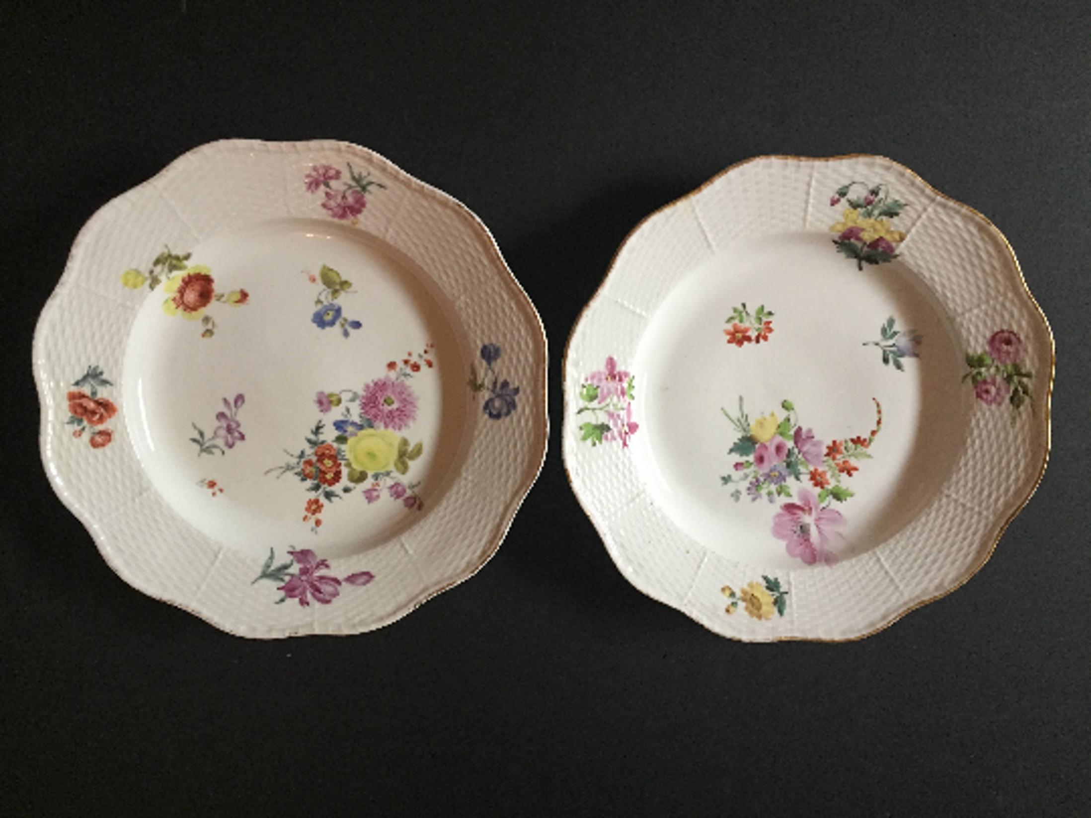 These dinner plates are beautifully decorated with a colorful mix of flowers. The borders have a molded basket-weave design framed with a thin gilt band on the scalloped rim edge. The center is decorated with hand painted polychrome enameled flower