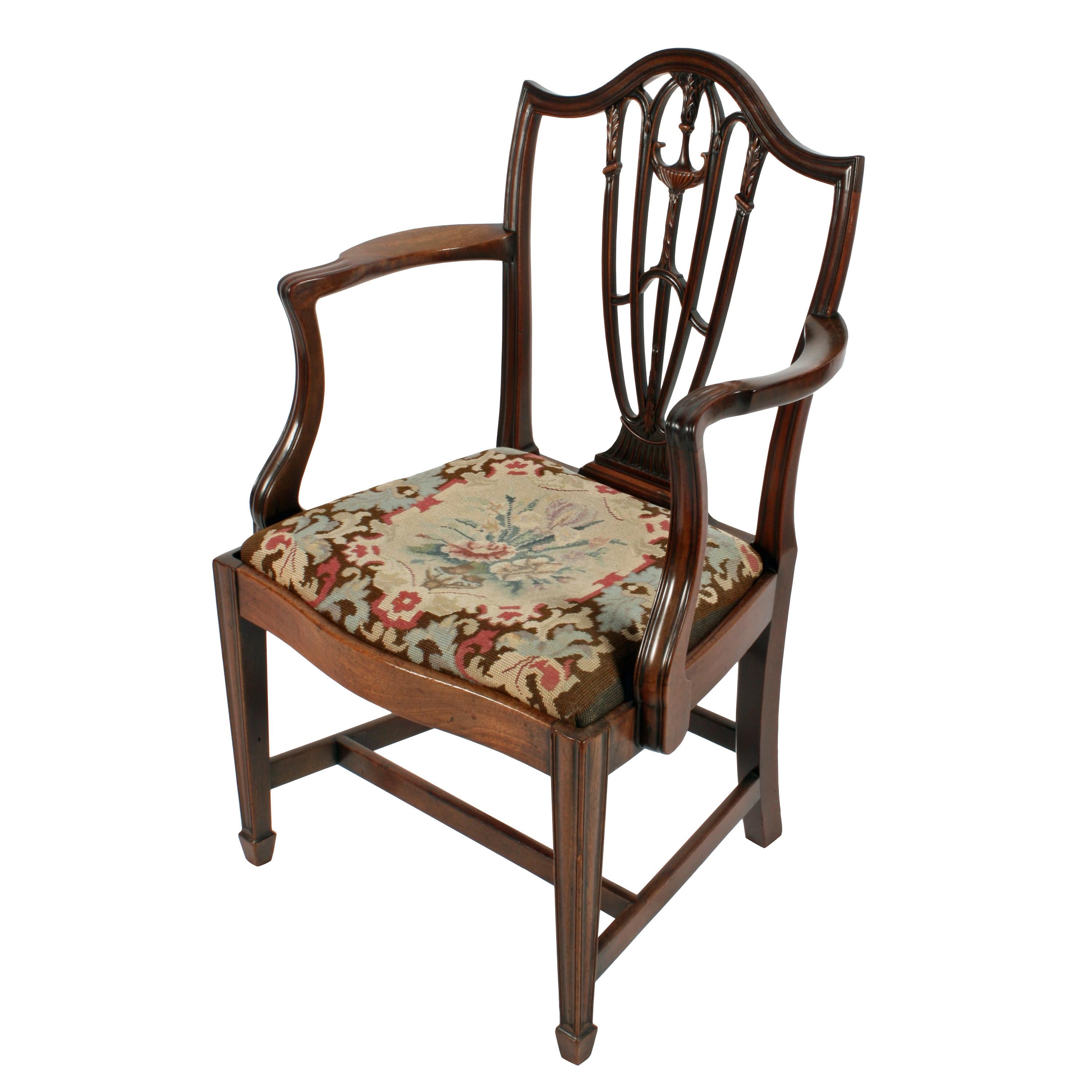 A late 18th century Georgian Hepplewhite mahogany elbow chair.

The chair has a domed top rail with a pierced and carved centre splat that is decorated with carved acanthus leaves and an urn.

The shaped arms have a swept support with a reeded