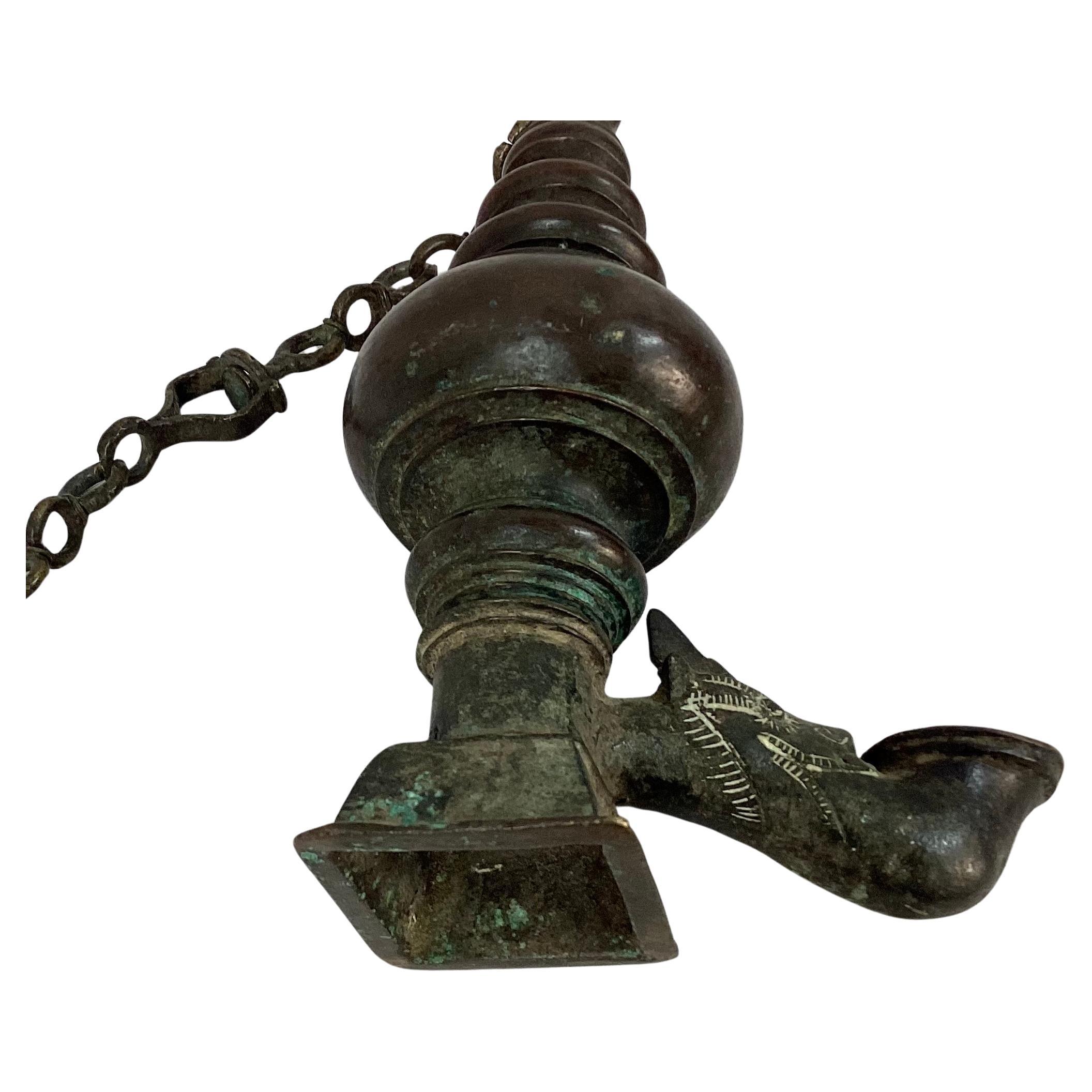 18th Century Sri Lankan hanging bronze oil lamp with Makara head spout. Solid bronze. Can be hung or used as a stand-alone decorating piece. Great piece to use with any decor.  Dimensions listed are including hanging bar. Oil lamp by itself is is